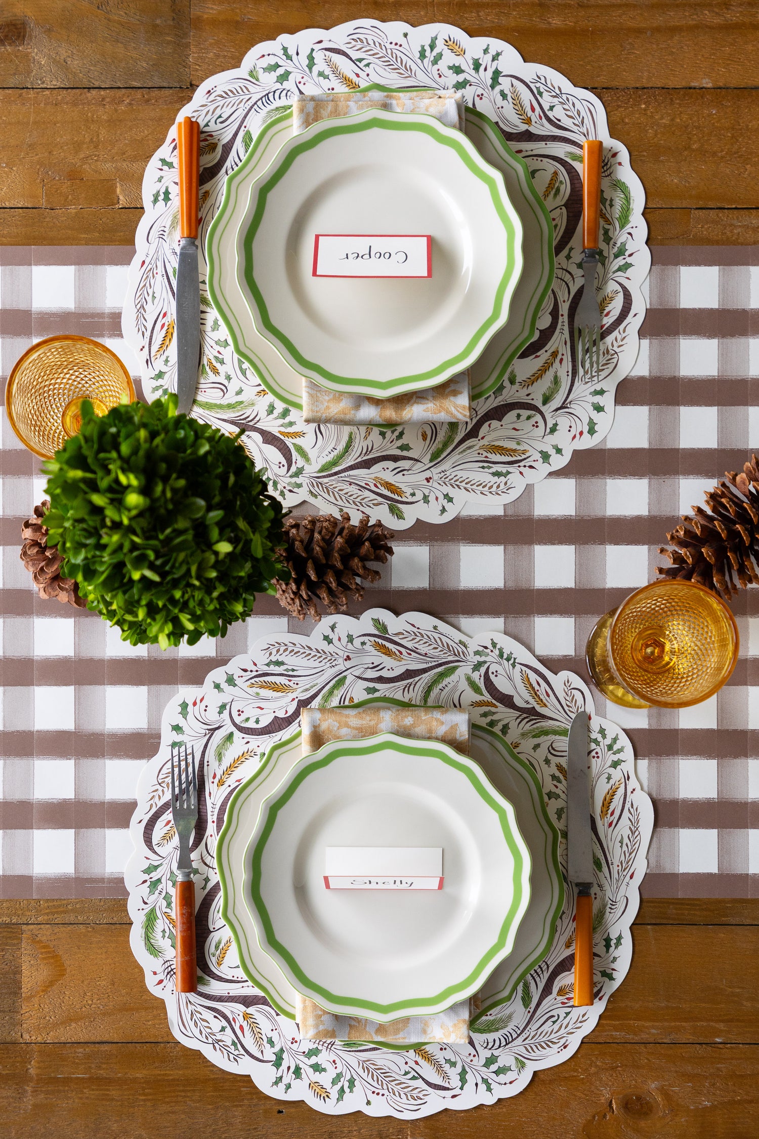Set of plates with decorative edges on a checkered tablecloth with pinecones and greenery.