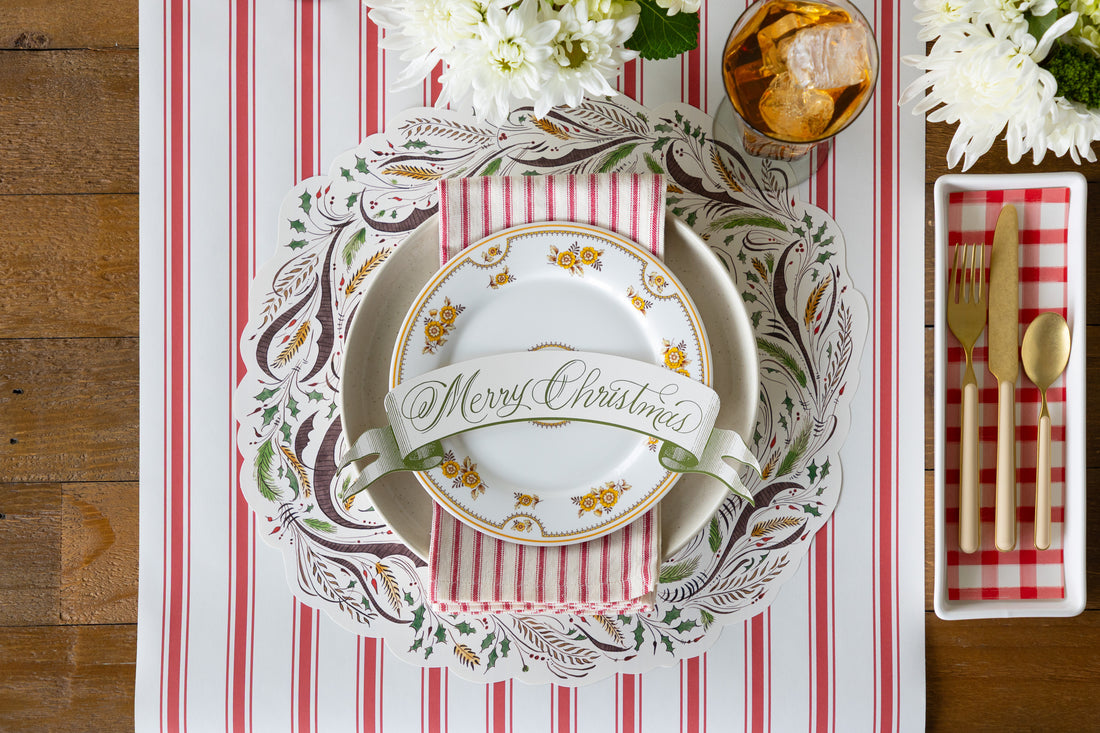 Placesetting with the Die-cut Merry Christmas Placemat on a red stripe table runner with vintage plates on it. 