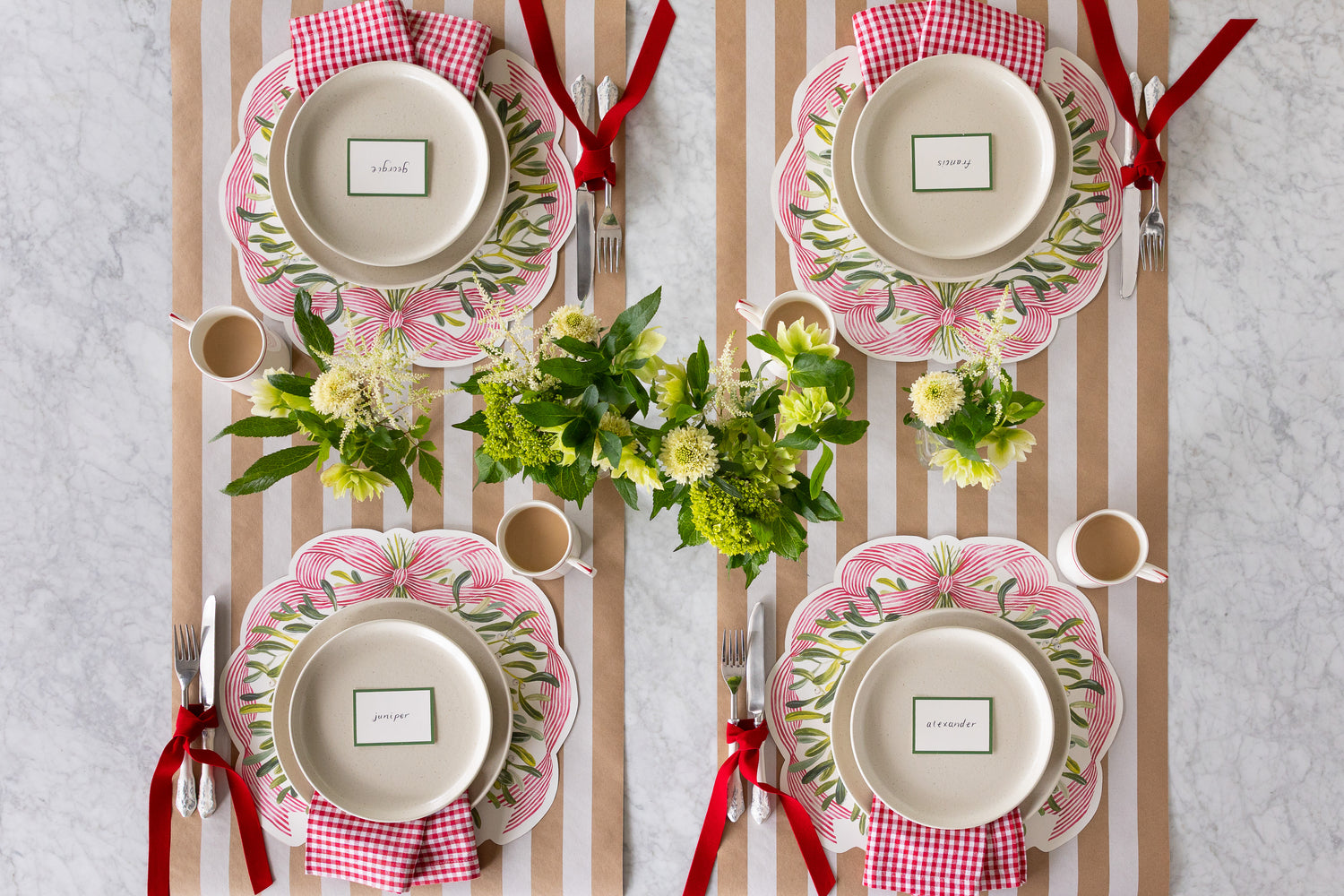 Festive tablesetting with Die-cut Mistletoe Placemats, a flower arrangement, white plates and a red ribbon tied around the cutlery. 