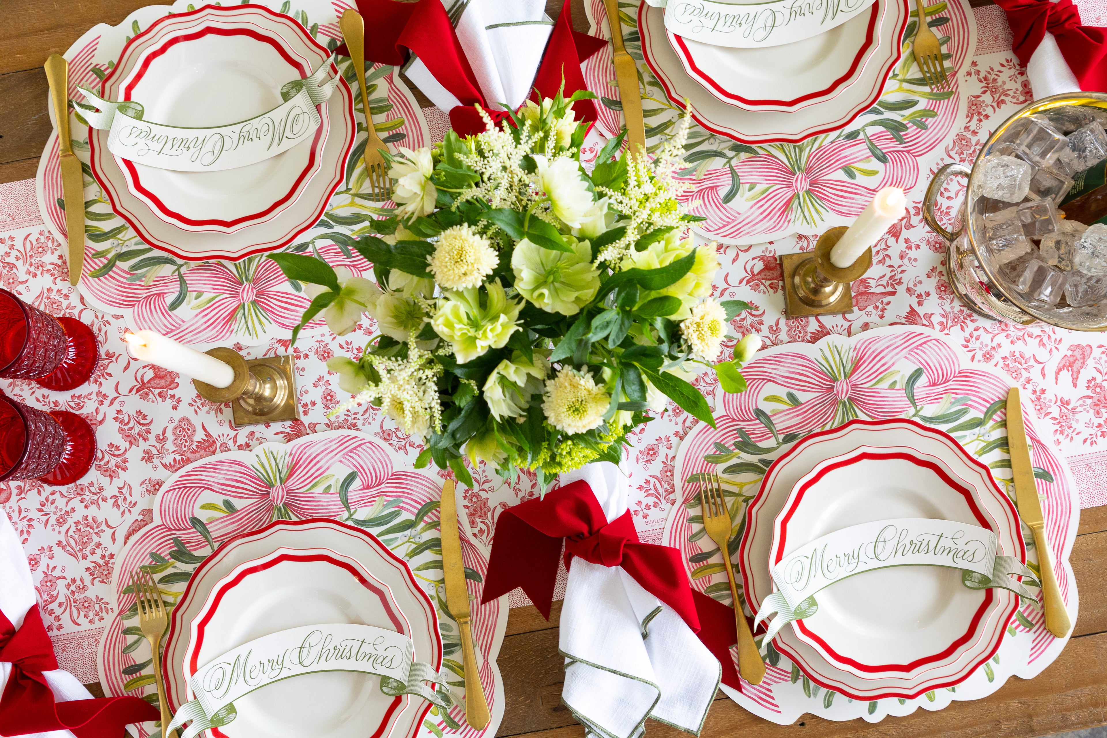 Festive tablesetting with Die-cut Mistletoe Placemats, a flower arrangement, white plates with red trim and candles. 
