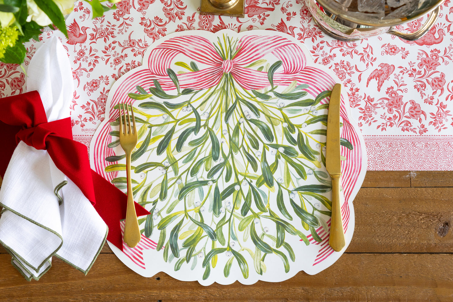 Decorative place setting with green leaf design on a table setting with red ribbon and white napkin.