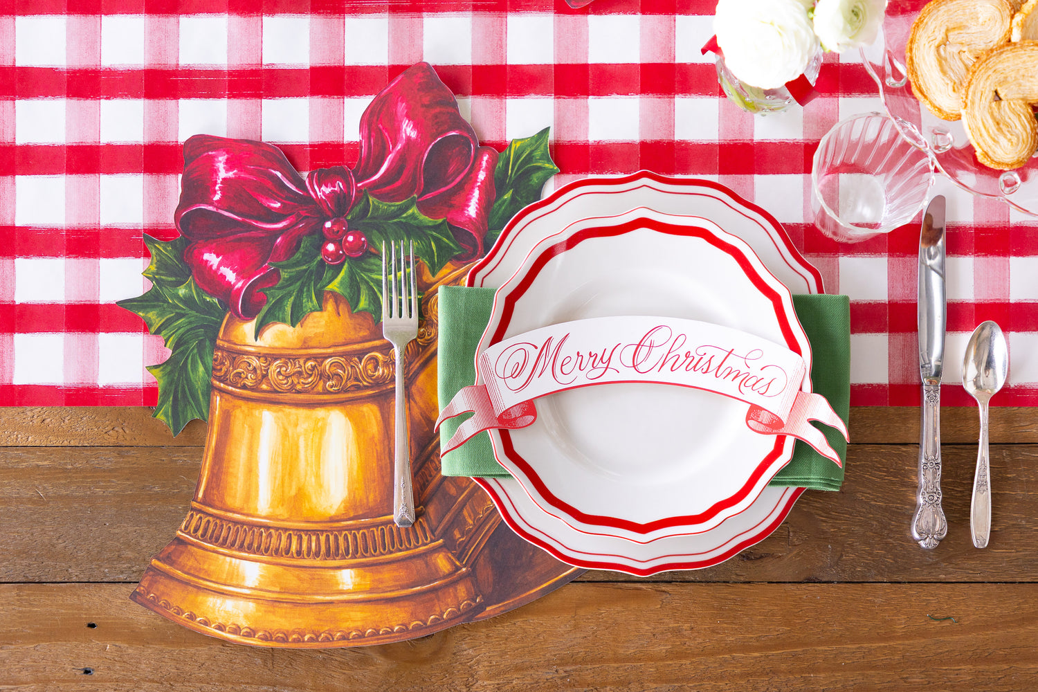 Festive table setting with the Die-cut Christmas Bells Placemat and a red plate, table banner and cutlery on it. 