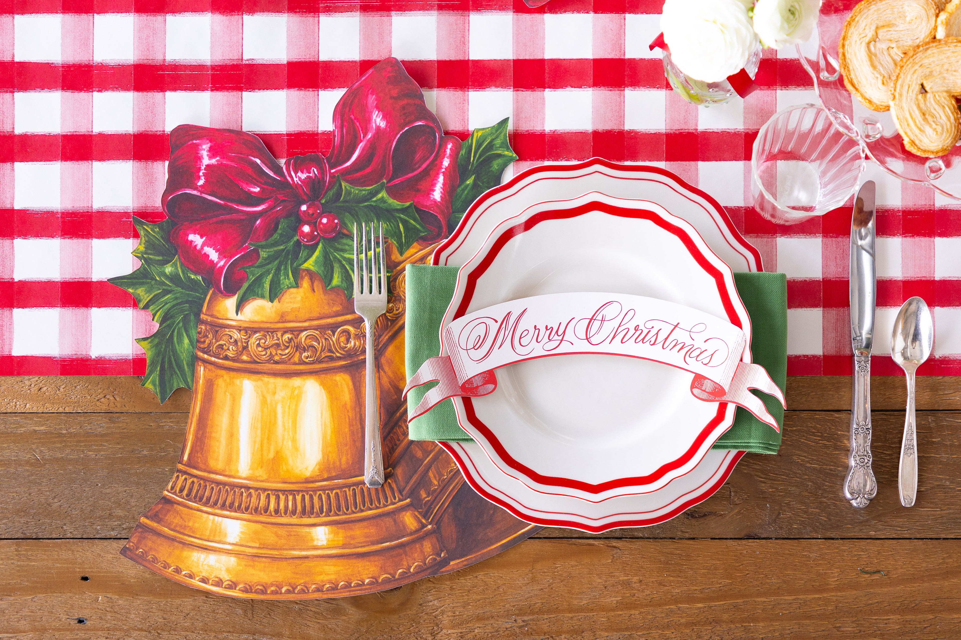 Festive table setting with the Die-cut Christmas Bells Placemat and a red plate, table banner and cutlery on it. 