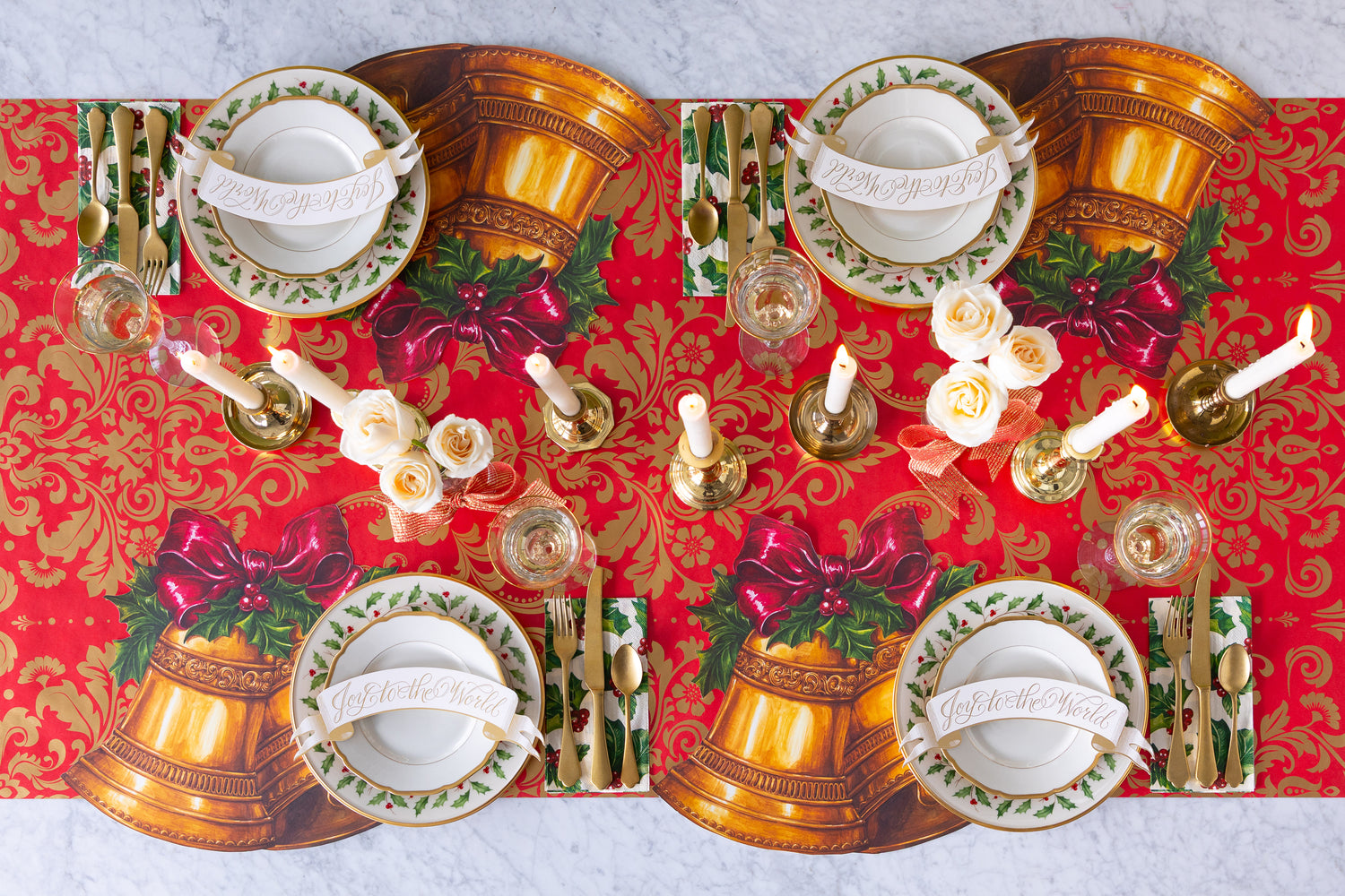 Decorative Christmas table setting with red runner, gold bells, and white candles.