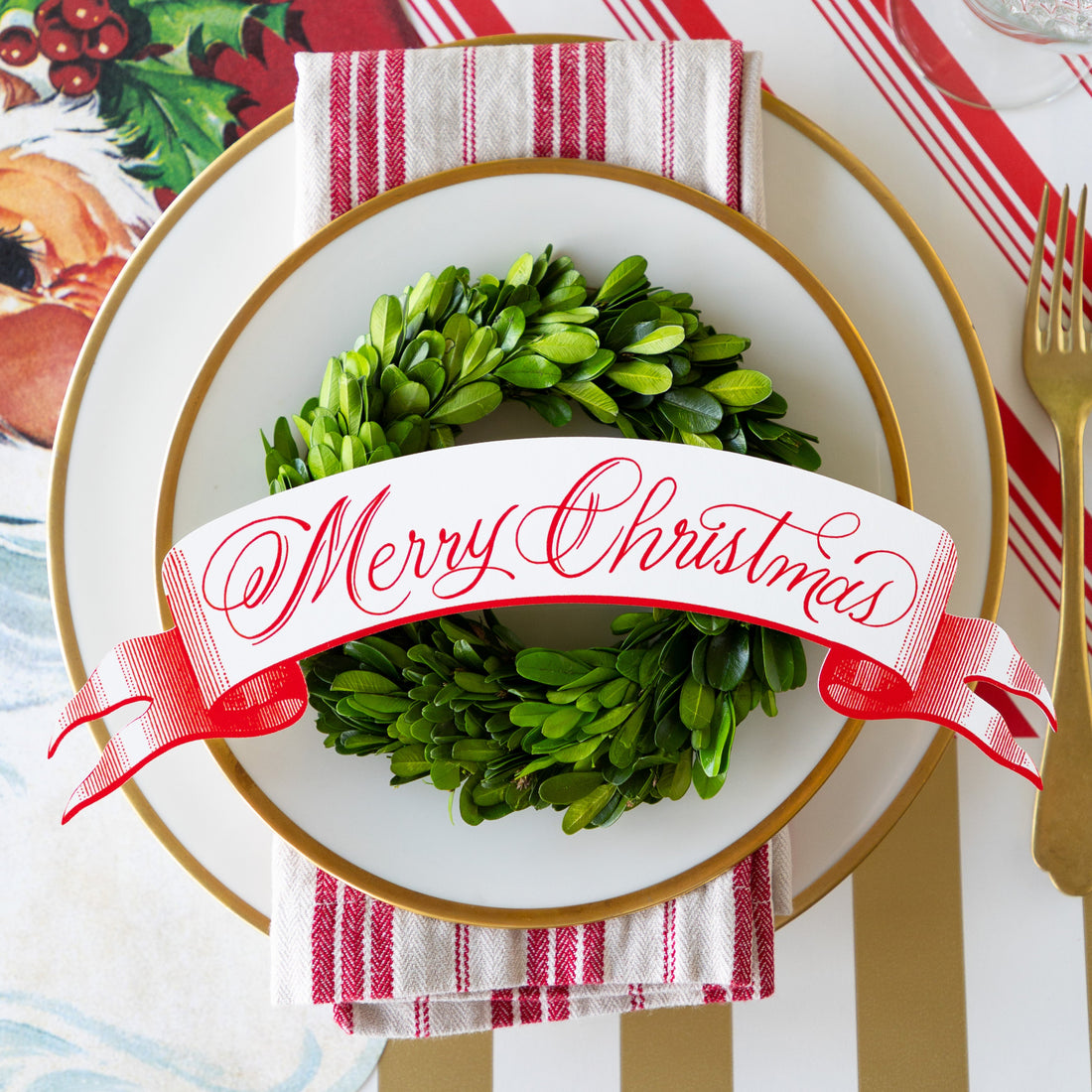 Christmas-themed place setting with a topiary wreath and Merry Christmas Table Banner Table Accent on a white plate.
