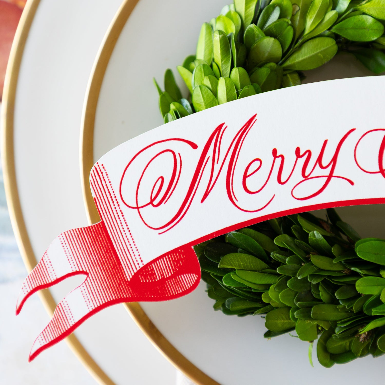 The Merry Christmas Banner Table Accent on a topiary wreath on a place setting.