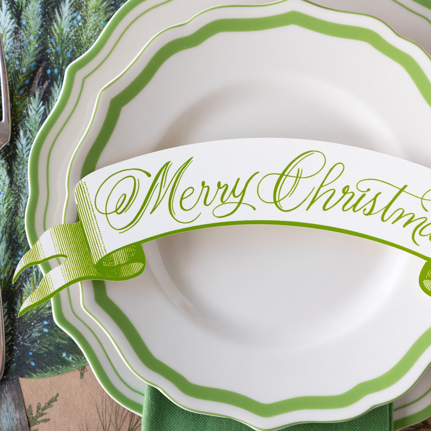 A close up of the Moss Merry Christmas Banner Table Accent atop green-and-white rimmed plates.