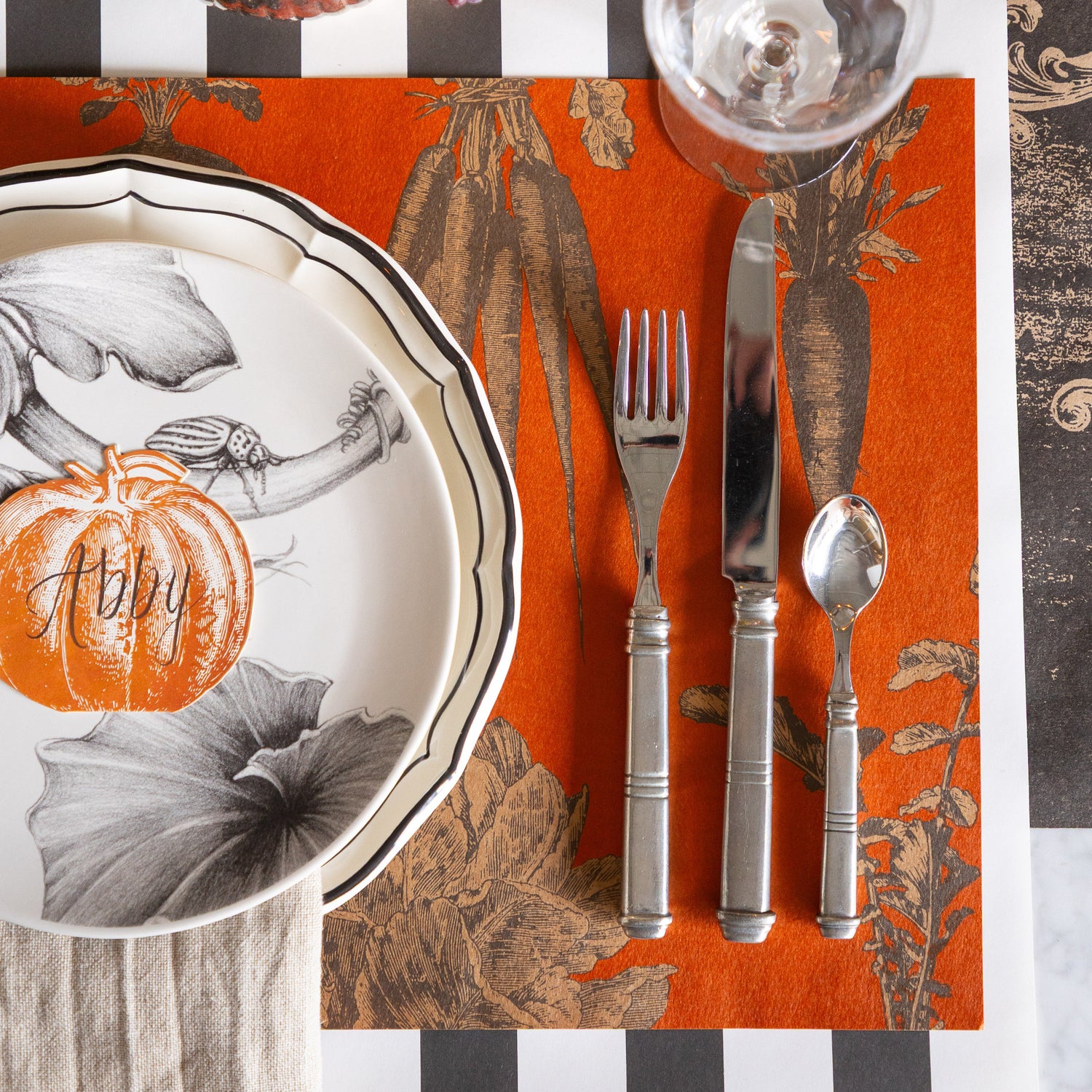 Halloween-themed place setting with decorative plate, silverware, and Harvest Vegetable (Persimmon) Placemat on the Black Classic Stripe Runner.