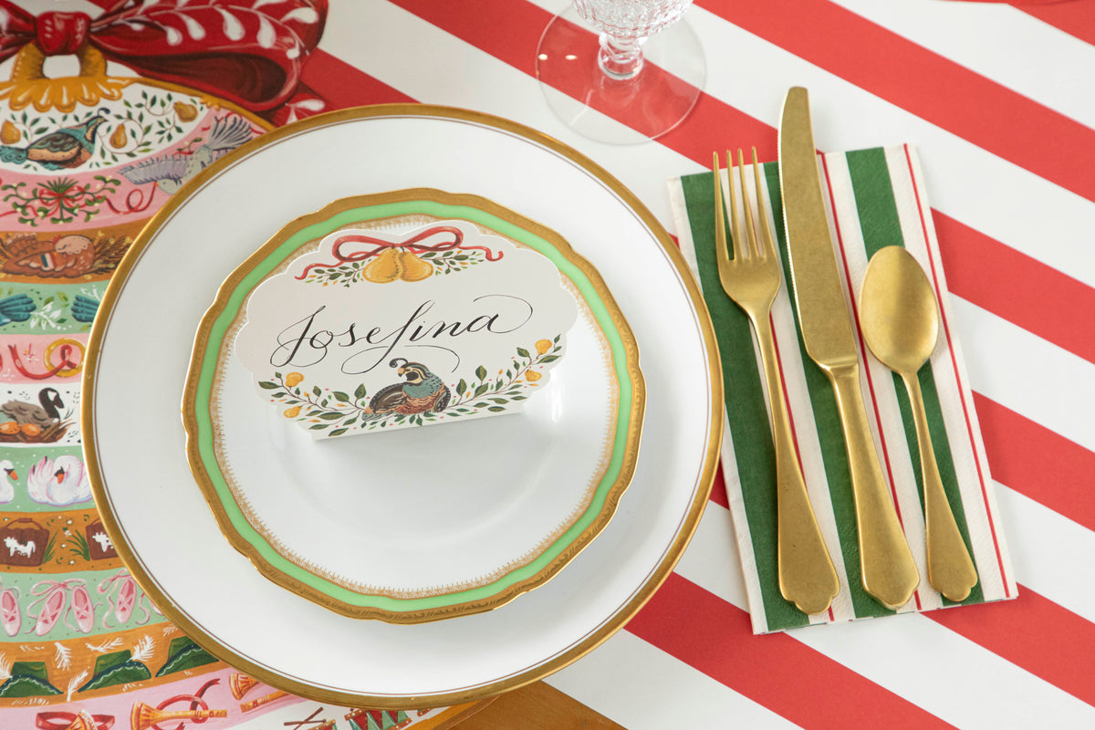 Description: A festive party table setting with plates, silverware, and Green &amp; Red Awning Stripe Napkins by Hester &amp; Cook.
