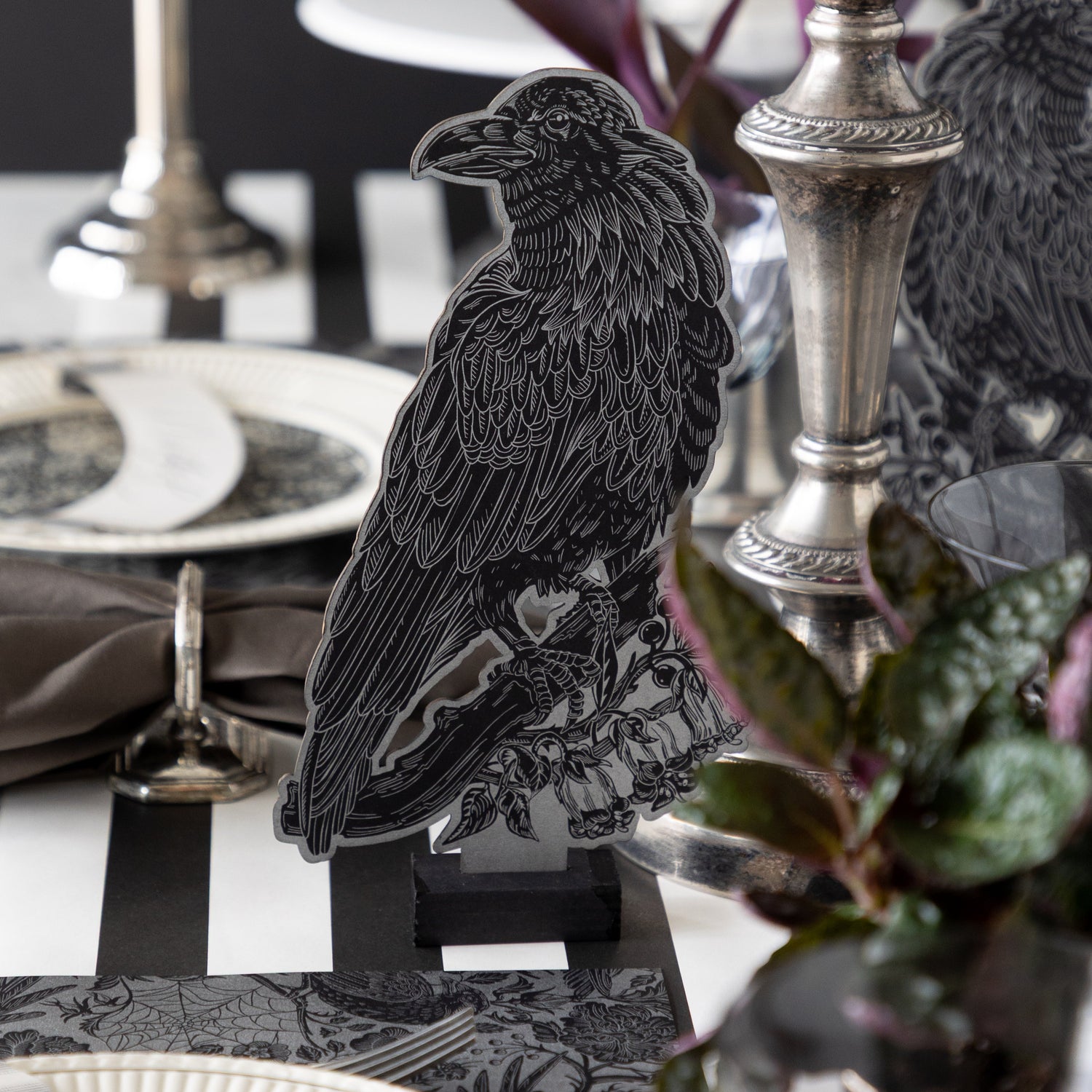 The Raven Table Ornament stands on a table surrounded by elegant tableware, silver candlesticks, and dark foliage.