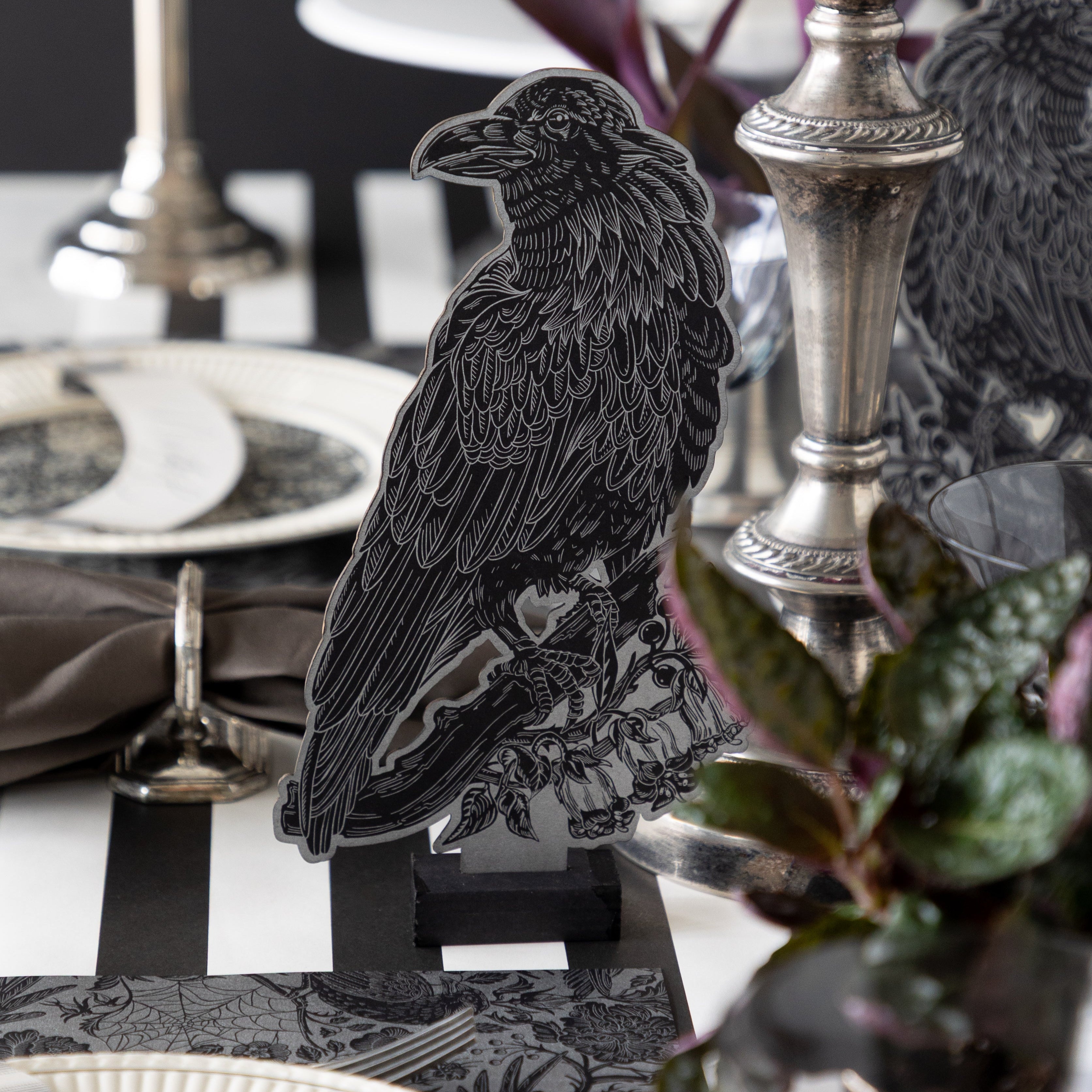 The Raven Table Ornament stands on a table surrounded by elegant tableware, silver candlesticks, and dark foliage.