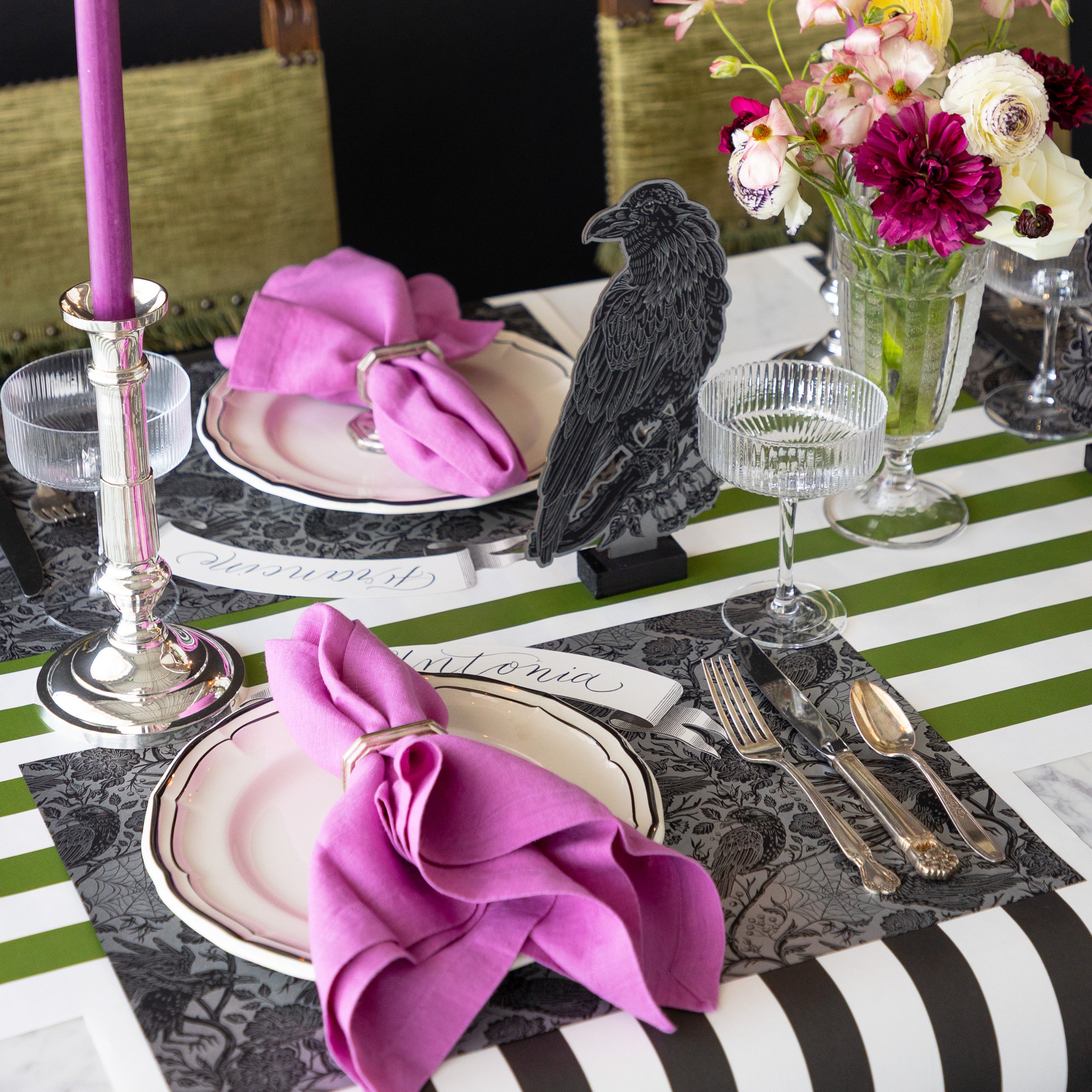 A table set with the Raven Toile Placemat, magenta napkins, silverware, coupe glasses, flowers, Raven Table Ornament, and Moss Green Classic Stripe Runner underneath.