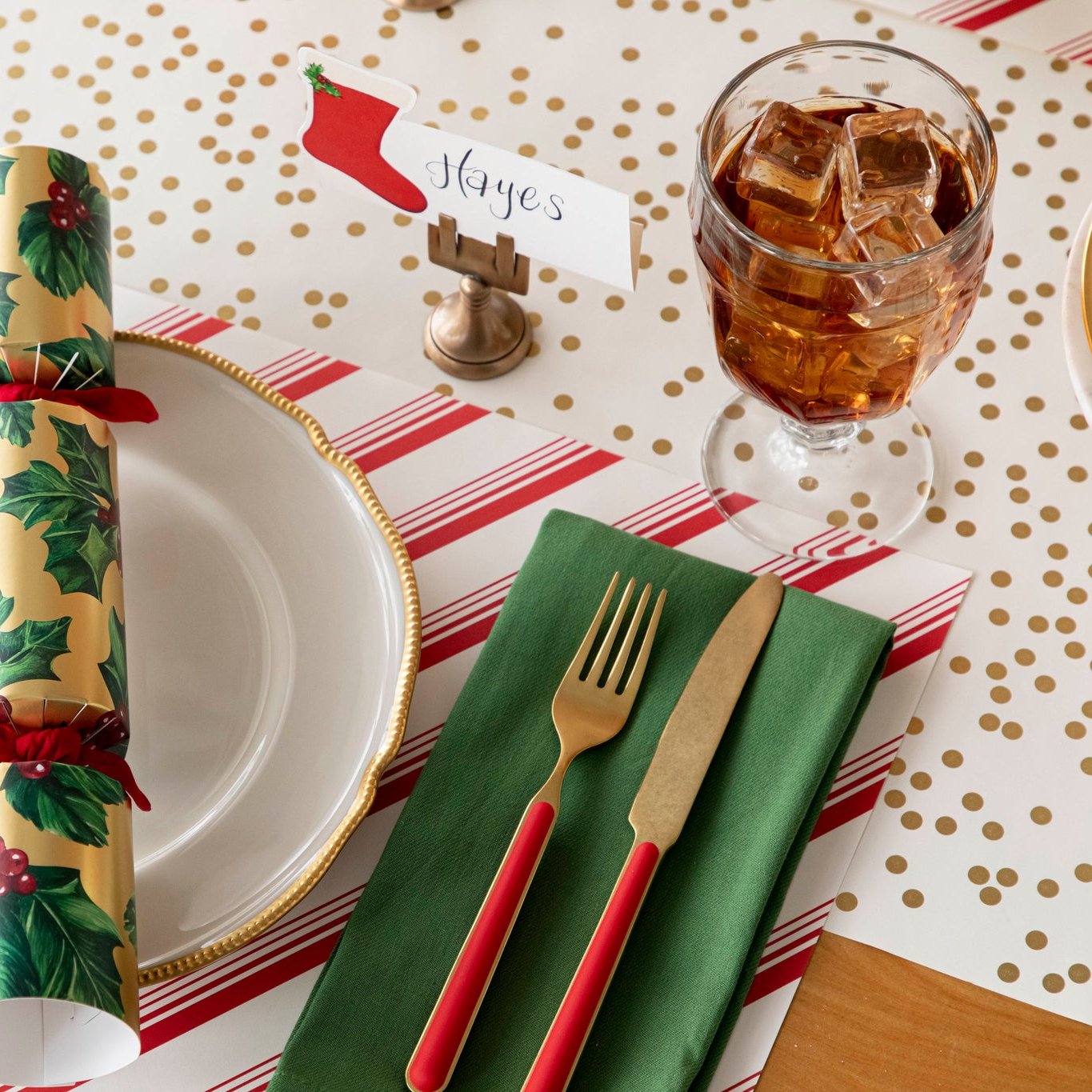 An elegant Christmas themed table setting featuring the Gold Confetti Runner under the Peppermint Stripe Placemat, dinnerware and the Gold Holly Cracker on top of a plate.