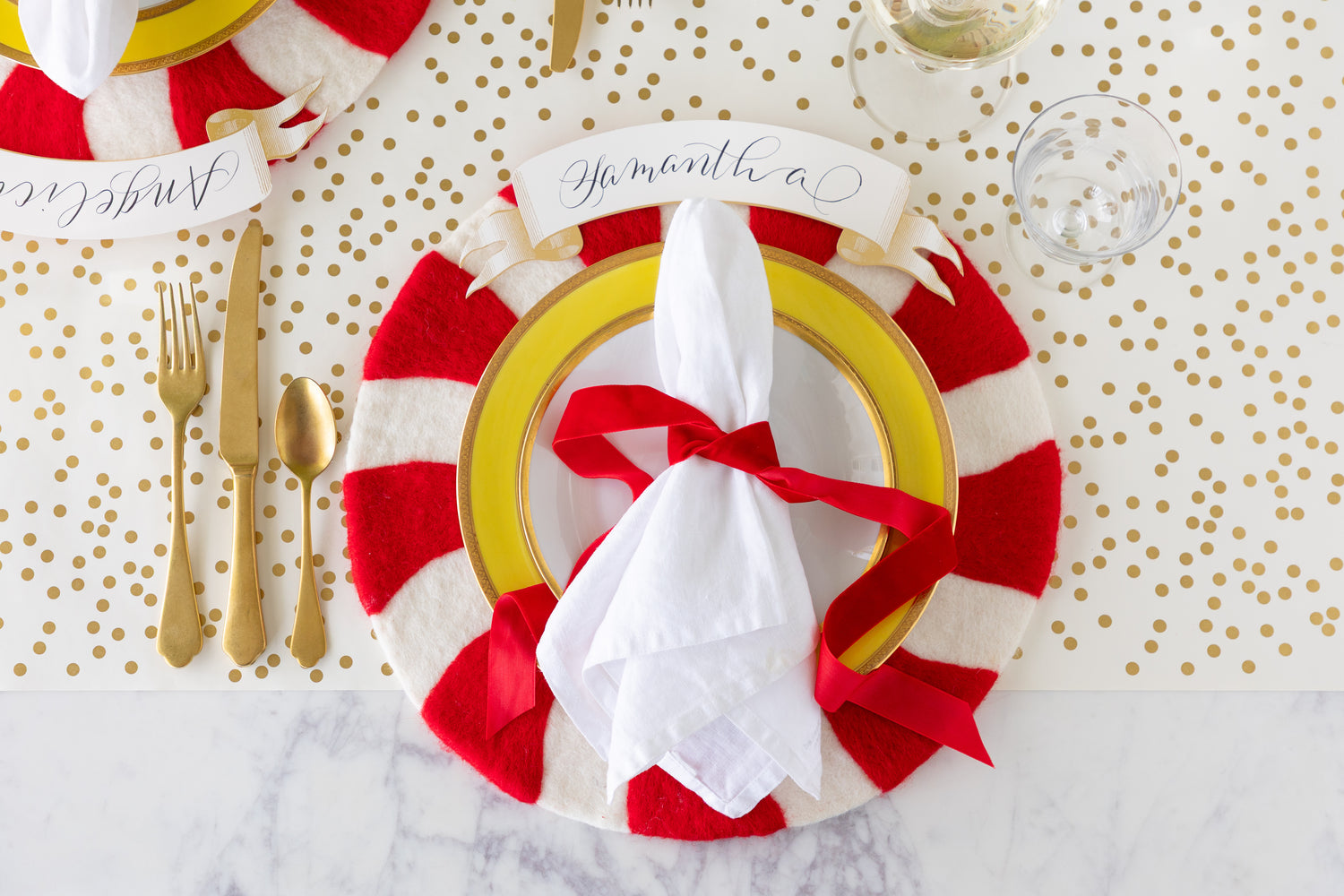 Festive place setting with a Candy Cane Felt Placemat that has a plate on it with a white napkin tied with a red ribbon on the Confetti Runner. 