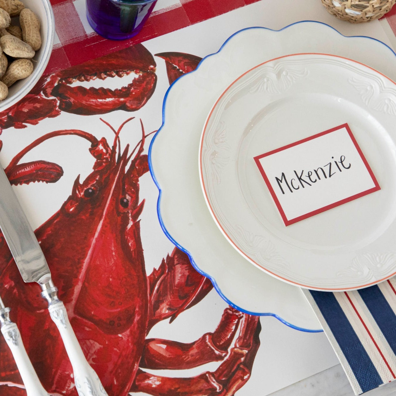 A nautical place setting featuring a Red Frame Place Card labeled &quot;McKenzie&quot; laying flat on the plate.