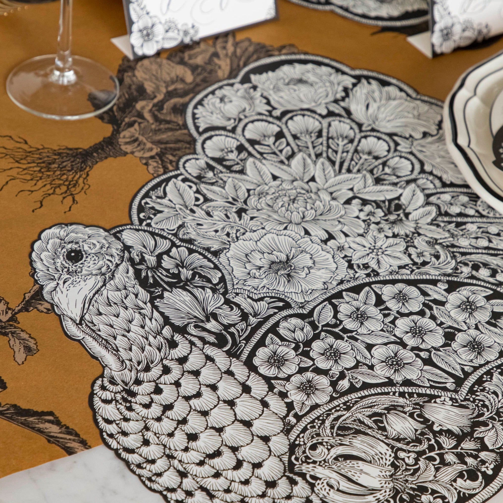 A Hester &amp; Cook die-cut Ebony Harvest Turkey Placemat on a black and white tablecloth, perfect for Thanksgiving and autumnal settings.