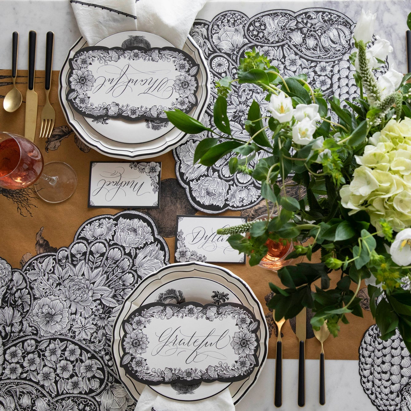 A black and white table setting with flowers and autumnal Die-cut Ebony Harvest Turkey Placemats by Hester &amp; Cook, perfect for a Thanksgiving gathering.