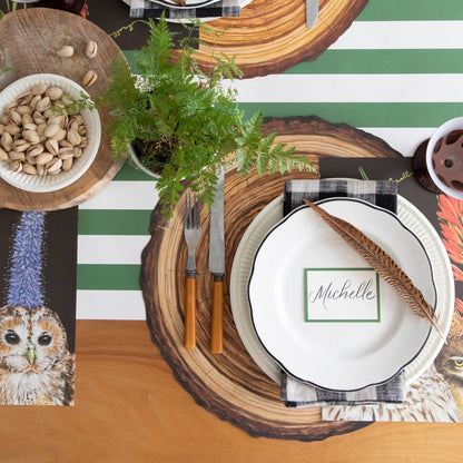 A forest themed table setting with a Die-cut Wood Slice Placemat and dinnerware on top and a Dark Green Classic Stripe Runner underneath.