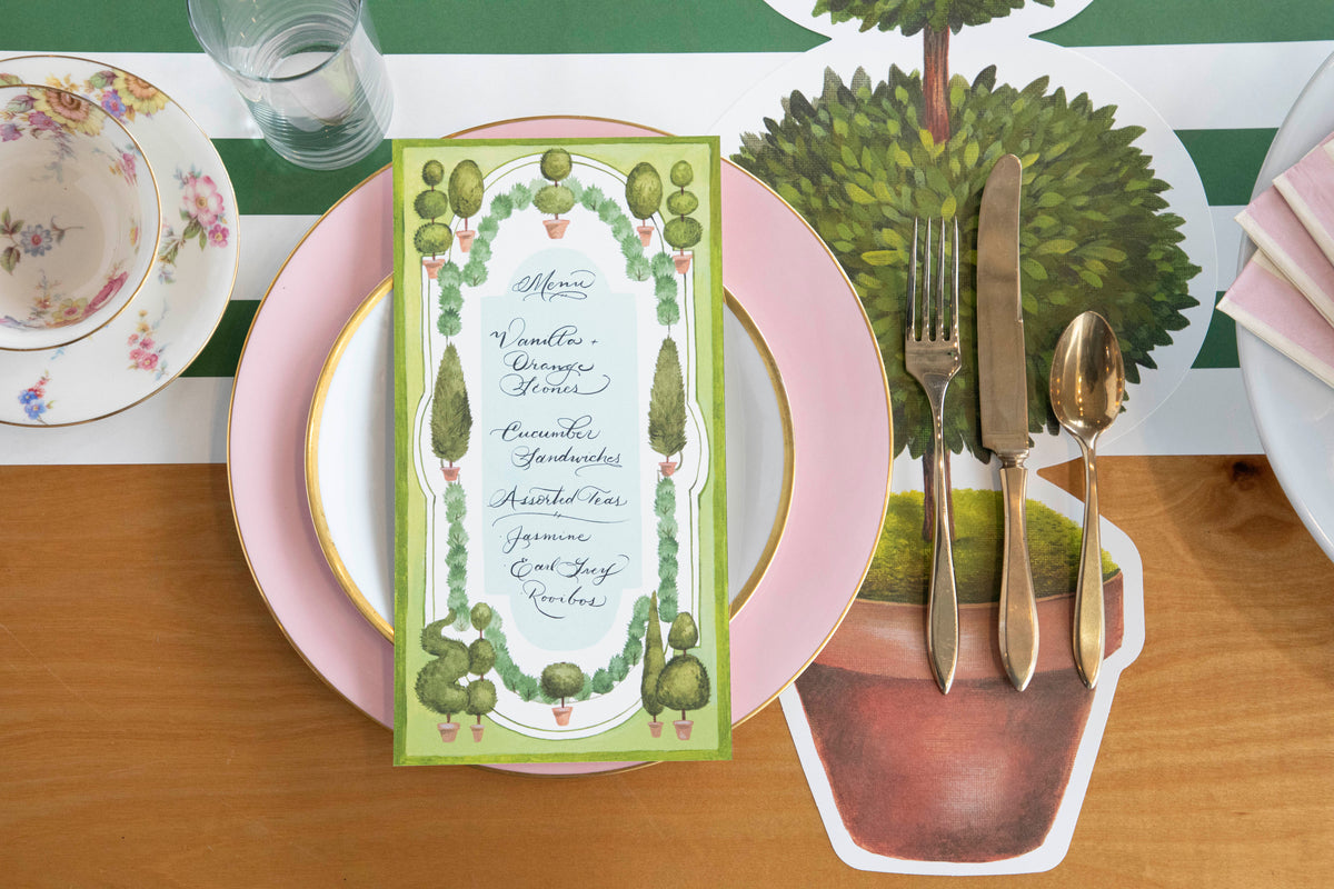 An elegant place setting featuring a Topiary Garden Table Card with a menu written on it resting on the plate, from above.