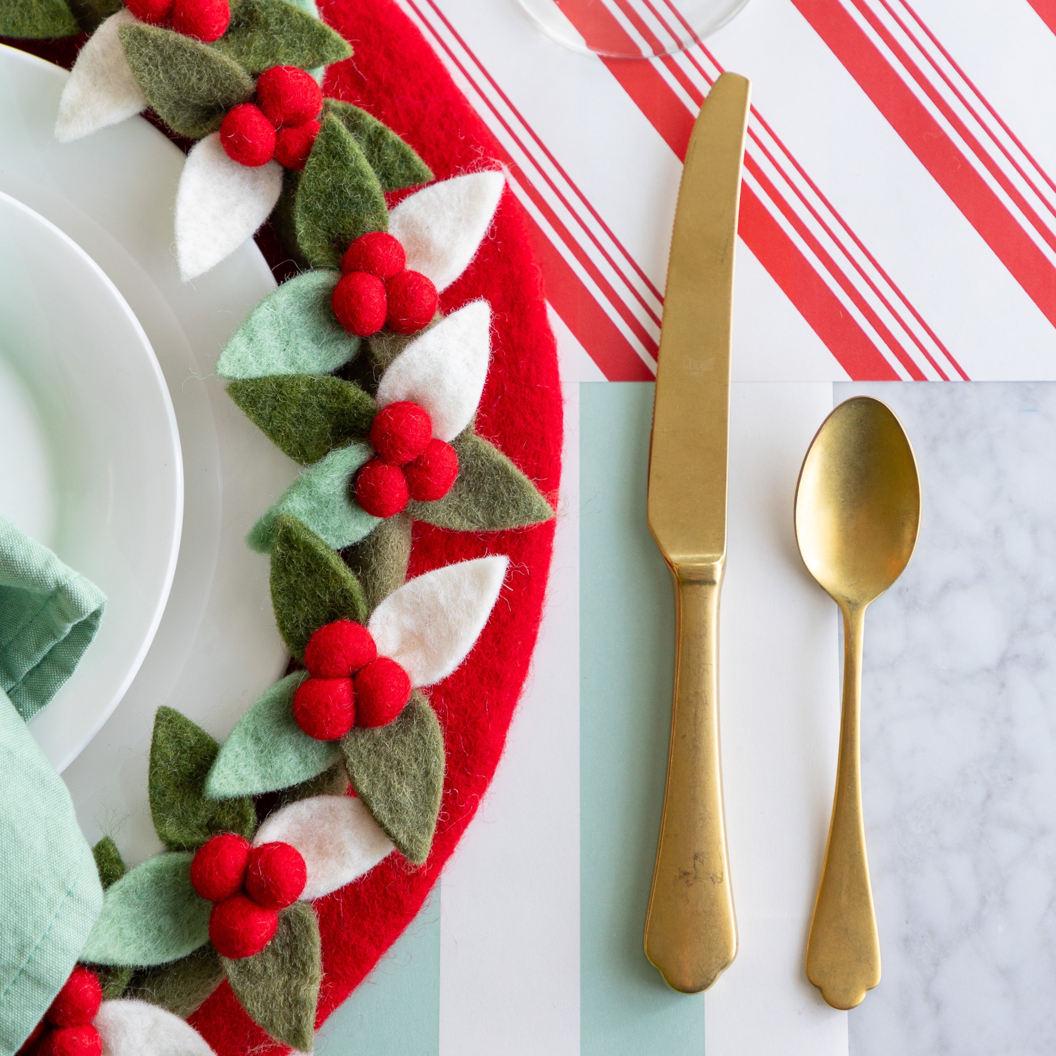 A place setting featuring the Red Felt Placemat with white plates and Felt Berry Charger atop and gold flatware beside, on the Peppermint Stripe and Seafoam Classic Stripe Runners.
