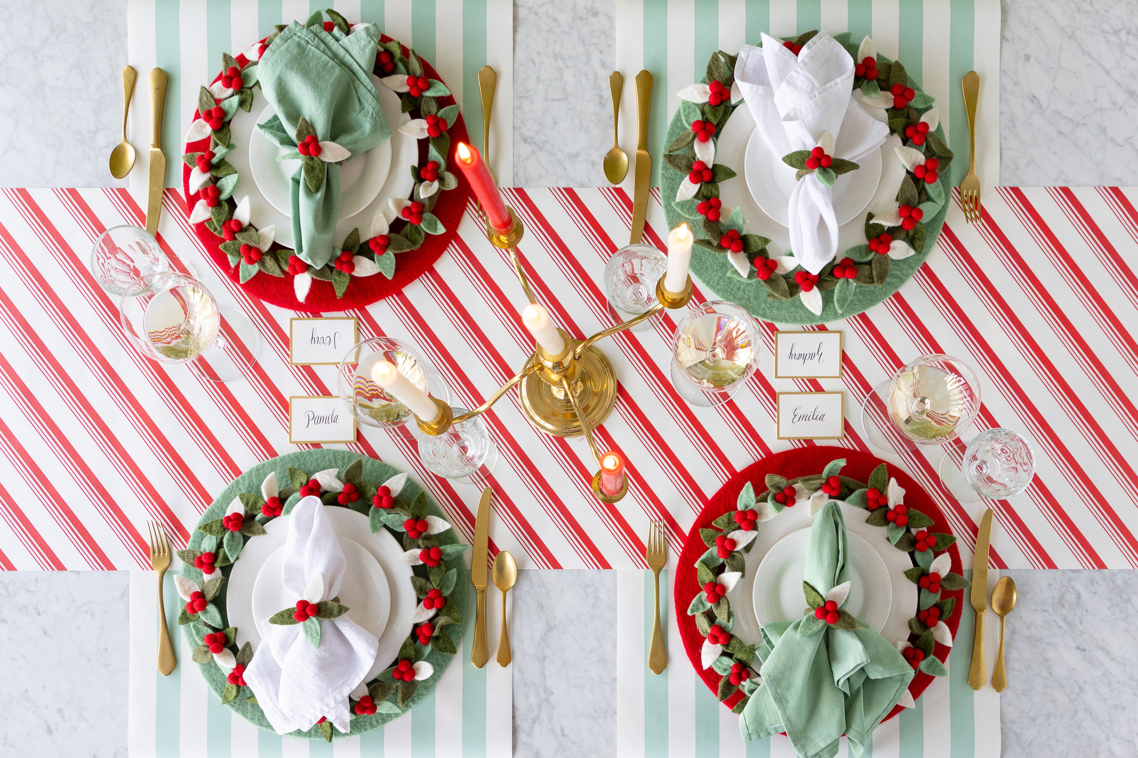 A Christmas table setting featuring a candleabra centerpiece, Red & Seafoam Felt Placemats, Gold Frame Place Cards, Holly Berry Felt Napkin Rings and gold flatware on the Peppermint Stripe Runner.