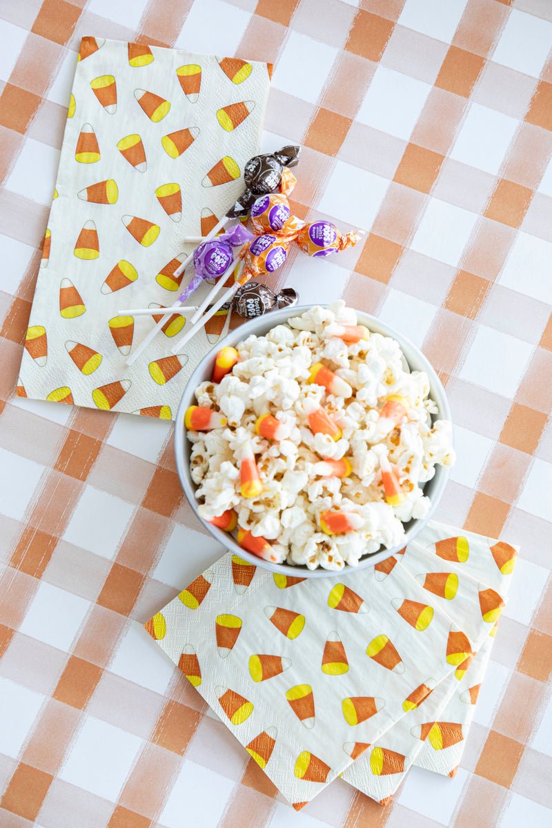 A top-down view of a Halloween treat table featuring a Candy Corn Guest Napkin and three Candy Corn Cocktail Napkins fanned out on the table. 