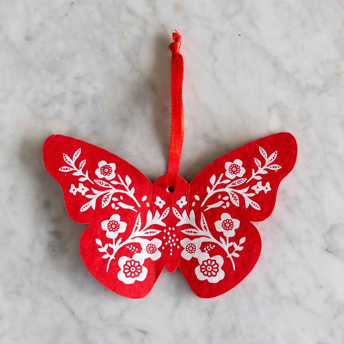 Red butterfly-shaped ornament with white floral patterns on a marble surface.