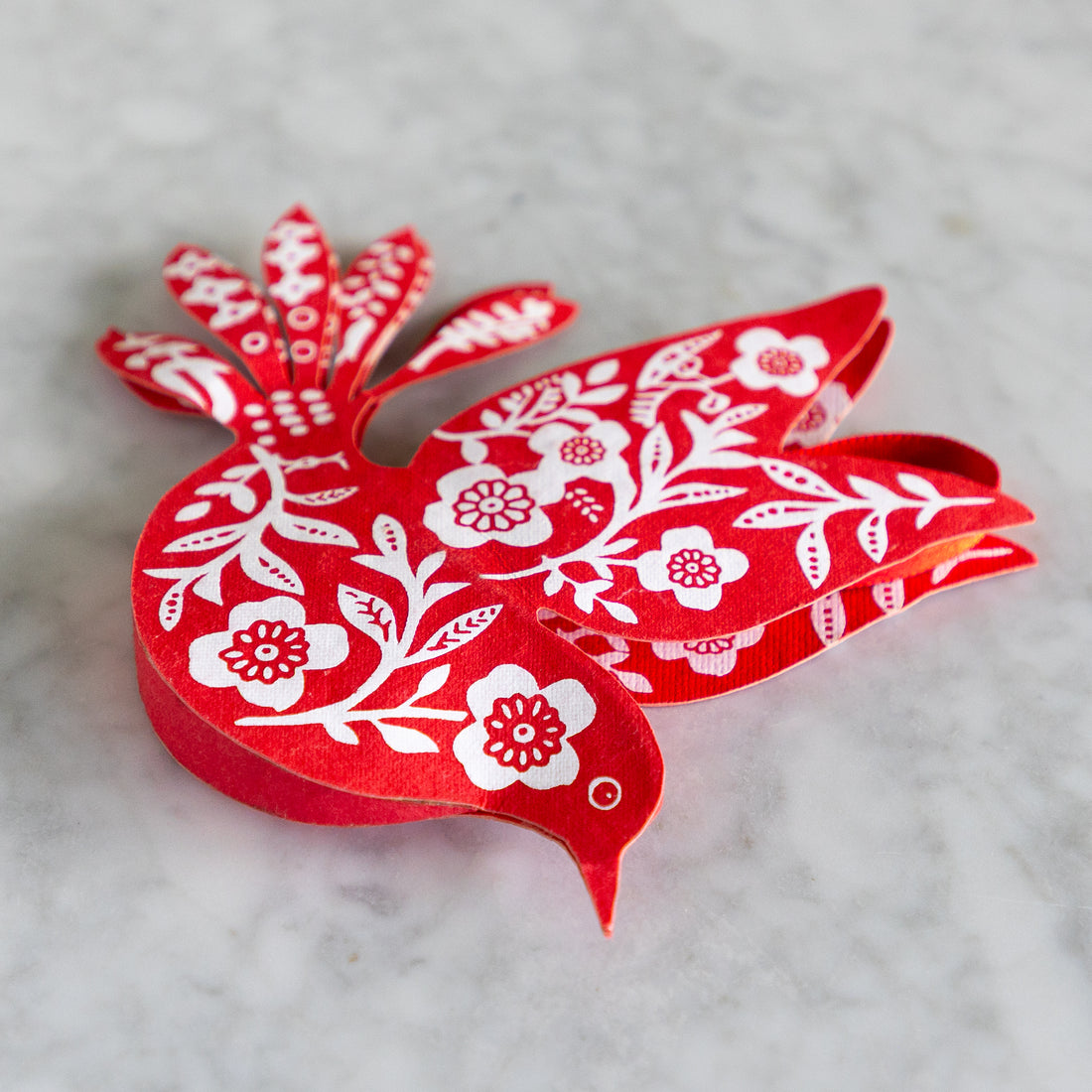 Red paper cutout of a dove with white floral patterns on a marble surface.
