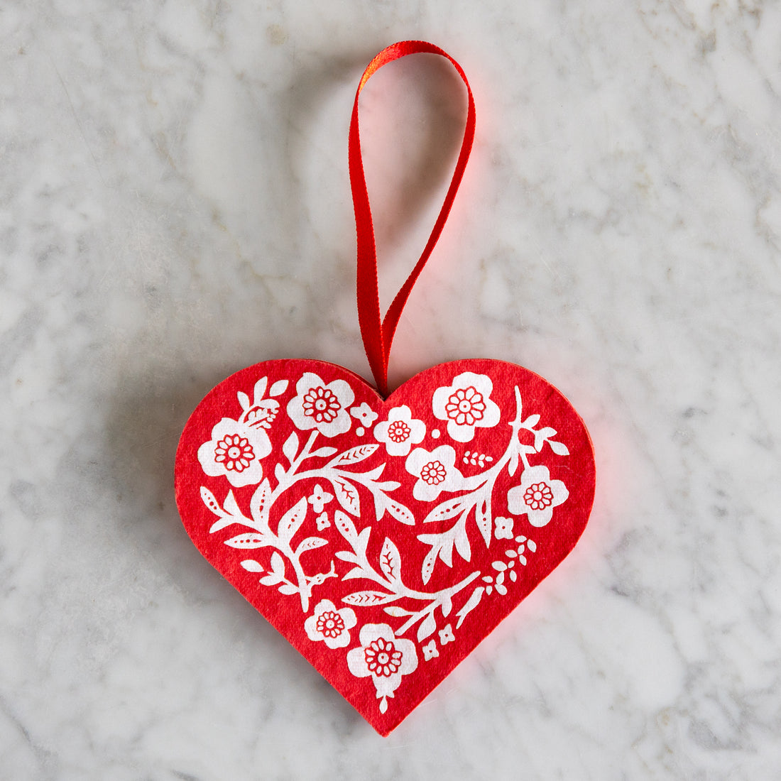 Red heart-shaped ornament with white floral patterns on a marble surface.