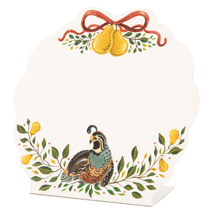 A white, die-cut, scalloped-edged freestanding place card featuring artwork of a partridge and golden pears adorning the top and bottom edges of the card.