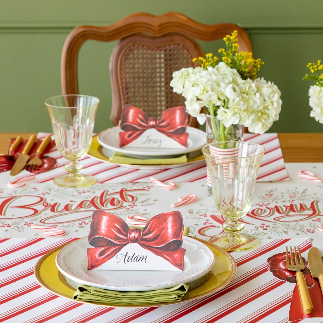 The Bow Place Card with &quot;Adam&quot; written on it, on a festive table setting for two.