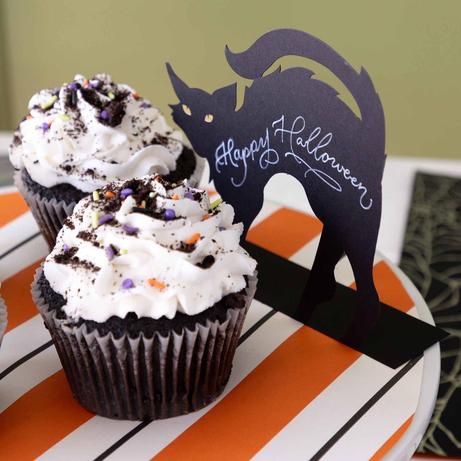 Black Cat Place Card reading "Happy Halloween" on a cake stand next to Halloween themed cupcakes.