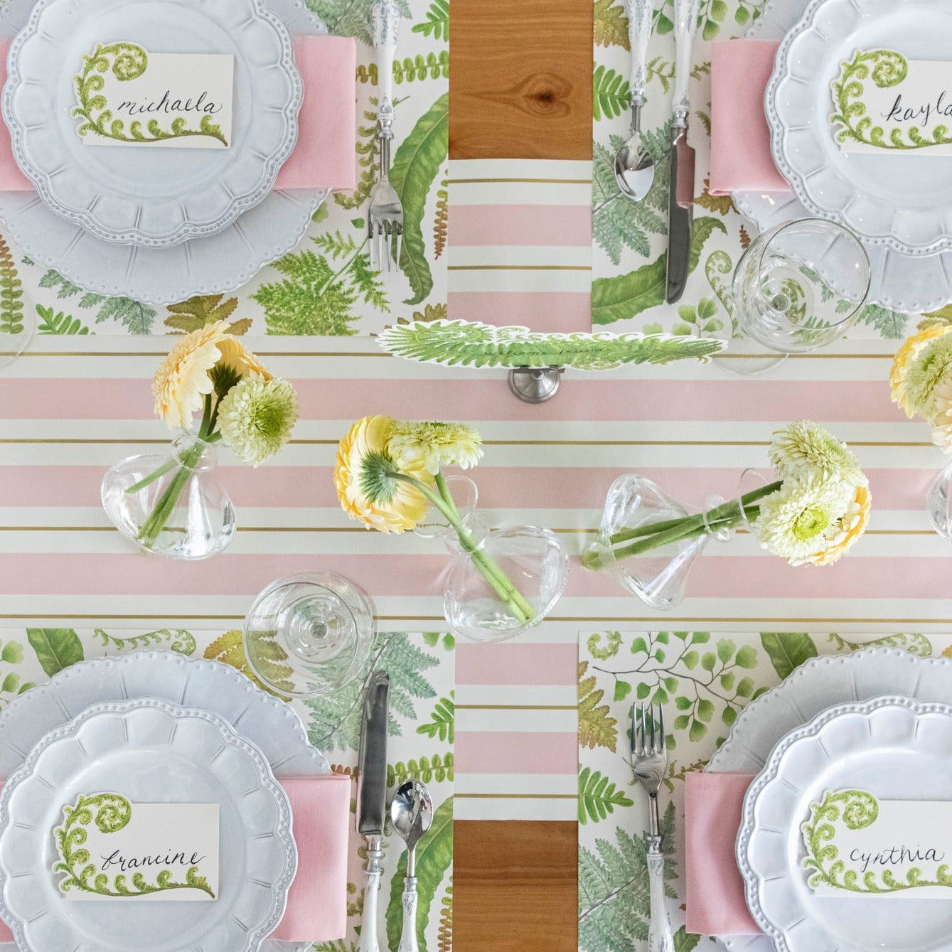 A table setting with pink and green plates and napkins, adorned with a Pink &amp; Gold Awning Stripe Runner from Hester &amp; Cook.