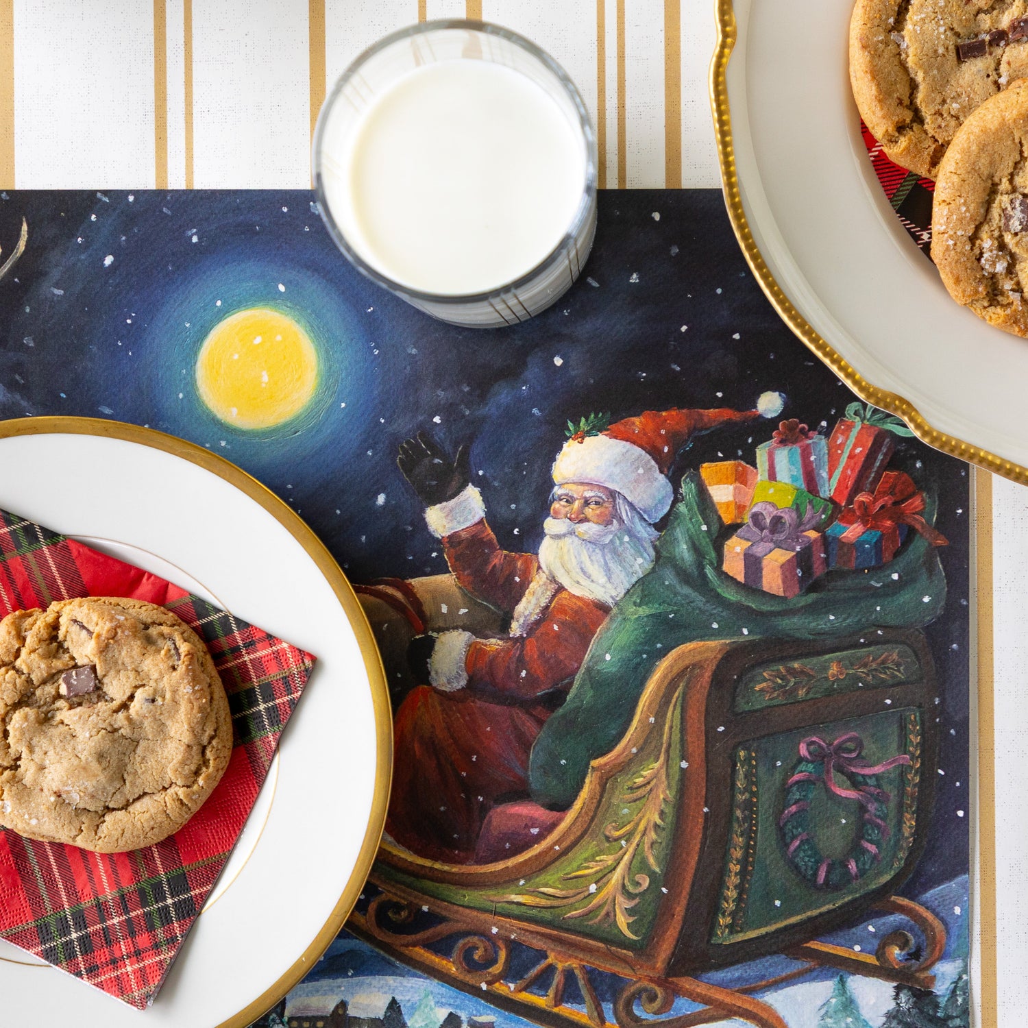 A place setting featuring the Sleigh Ride Placemat with a plate, napkin and cookie, atop, a glass of milk, a plate of cookies nearby and Antique Gold Stripe Runner underneath.