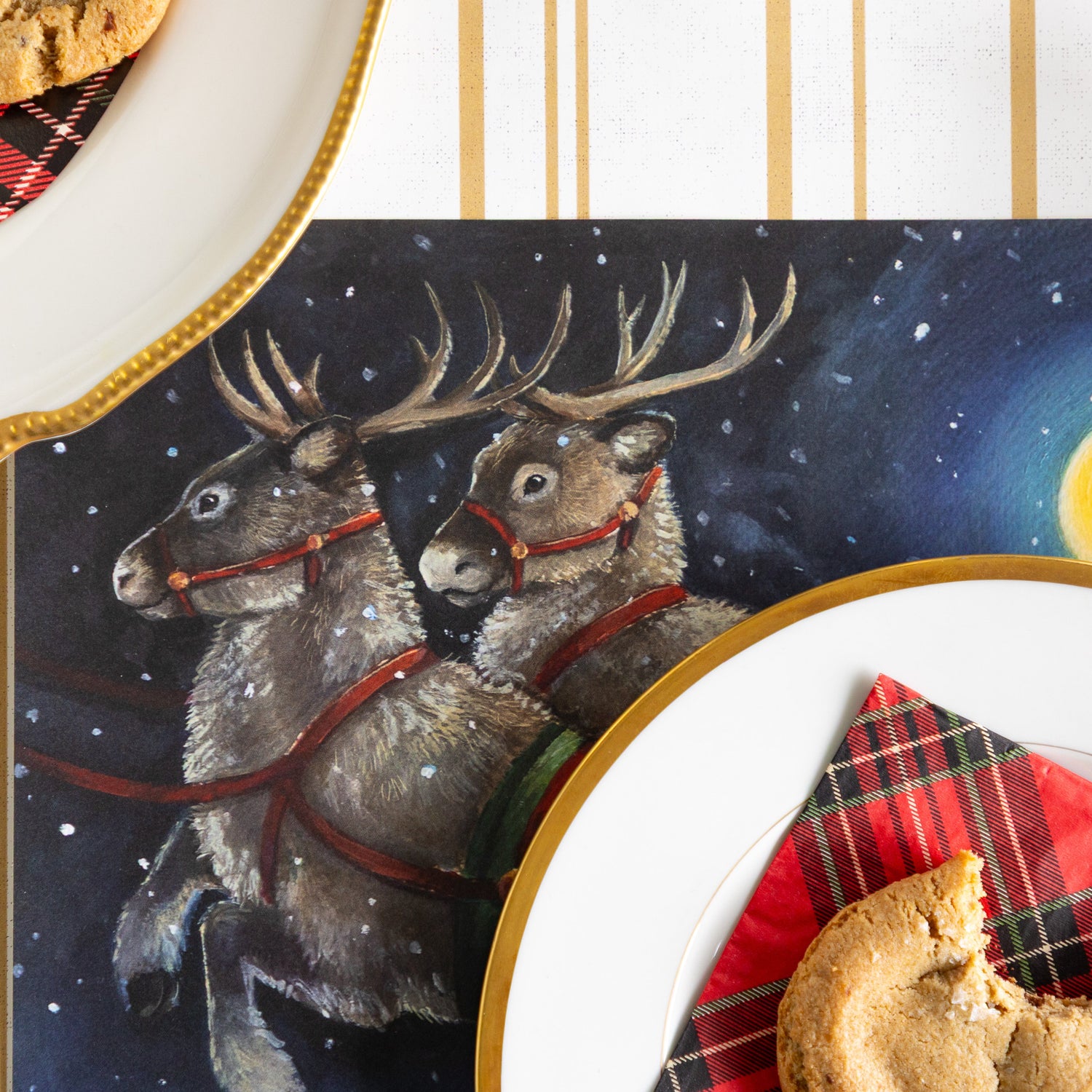 A close up of the Sleigh Ride Placemat showing the reindeer in the night sky, under a plate with a napkin and cookie atop,