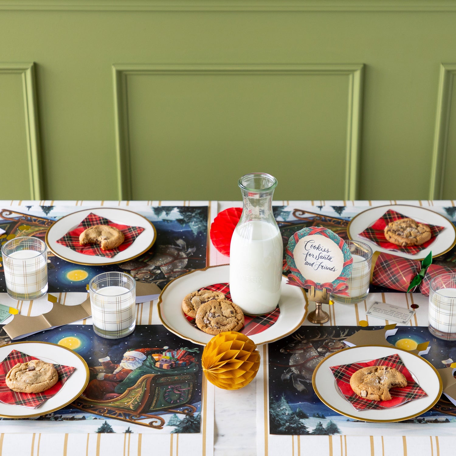 A Christmas table setting for four featuring the Sleigh Ride Placemat, plates of cookies with a napkin and glasses of milk atop, a plate of cookies and a jar of milk in the center, and Antique Gold Stripe runner underneath.