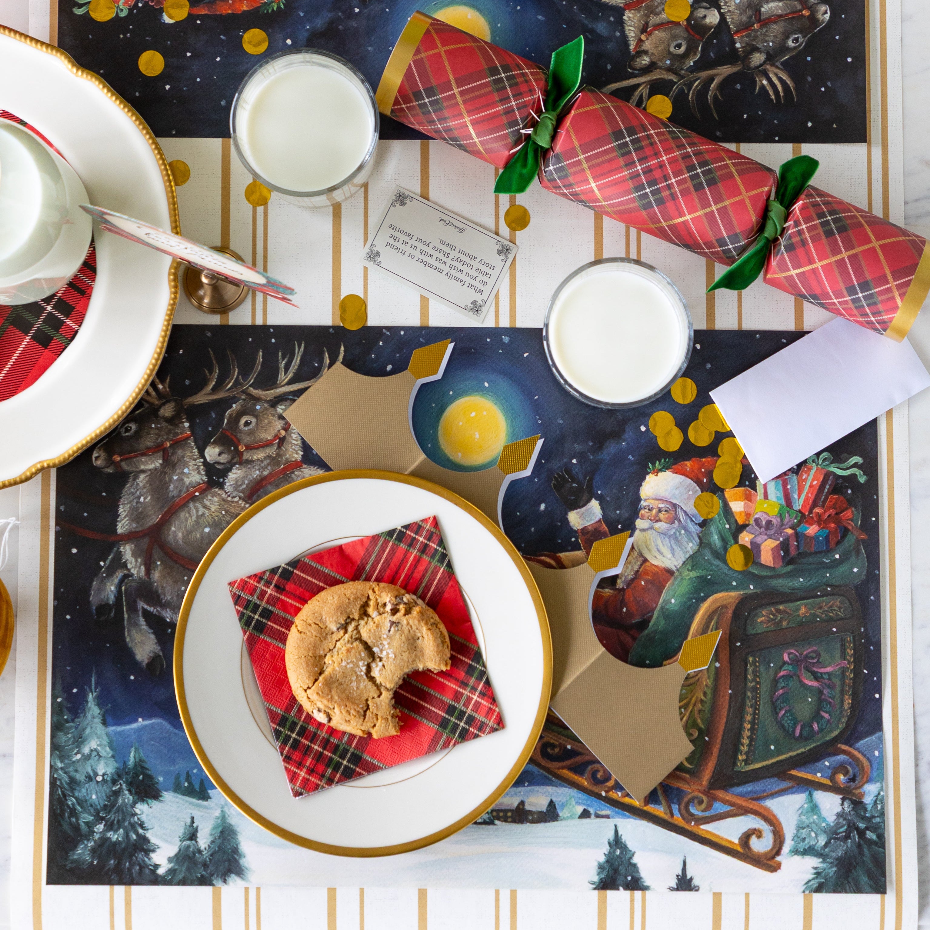 A Christmas table setting featuring the Sleigh Ride Placemat with a gold rimmed plate, Red Plaid Cocktail Napkin and bitten cookie atop, a glass of milk, Red Plaid Cracker nearby and Antique Gold Stripe Runner underneath.