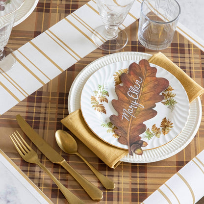 A table setting with the Autumn Plaid Placemat with a plate and brass flatware, at a dynamic angle.