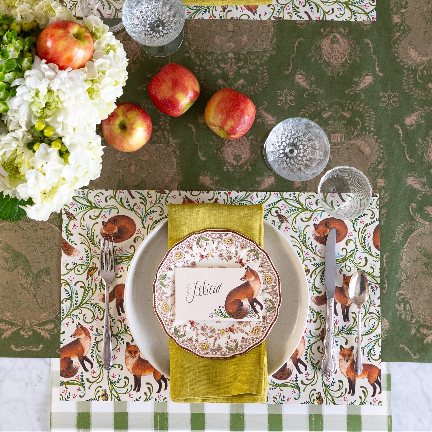 Fanciful Foxes Placemat on an elegant table setting with vintage dinnerware and silverware, Fanciful Fox Place Card with &quot;Felicia&quot; written on it, Moss Fable Toile Runner horizontally on the table and Moss Green Painted Check Runner vertically under the place setting.