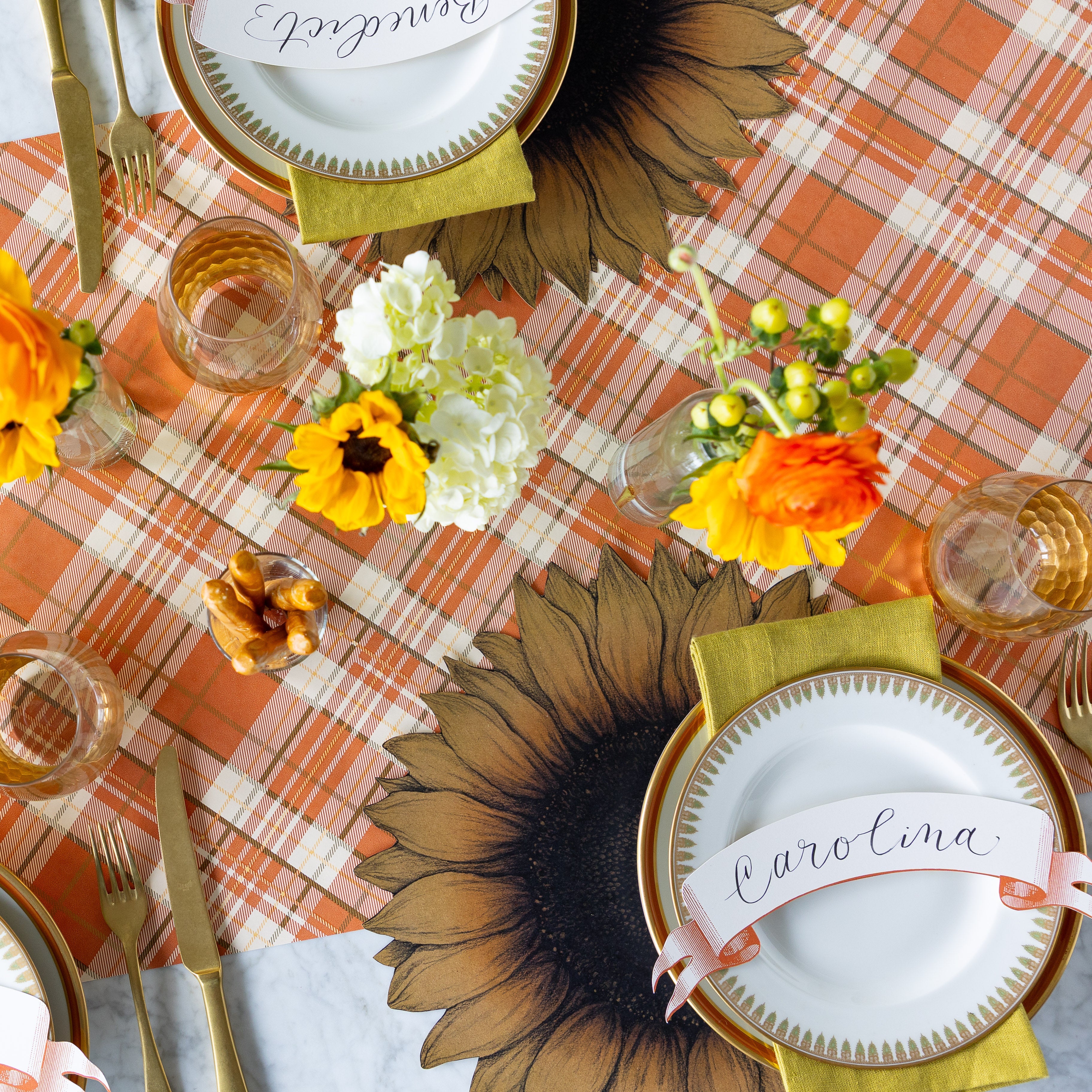 A charming table setting featuring the Die-cut Vintage Sunflower Placemat, gold-rimmed plate, green napkin, and a &quot;Carolina&quot; Orange Classic Banner Table Accent resting on the Autumn Plaid Runner.