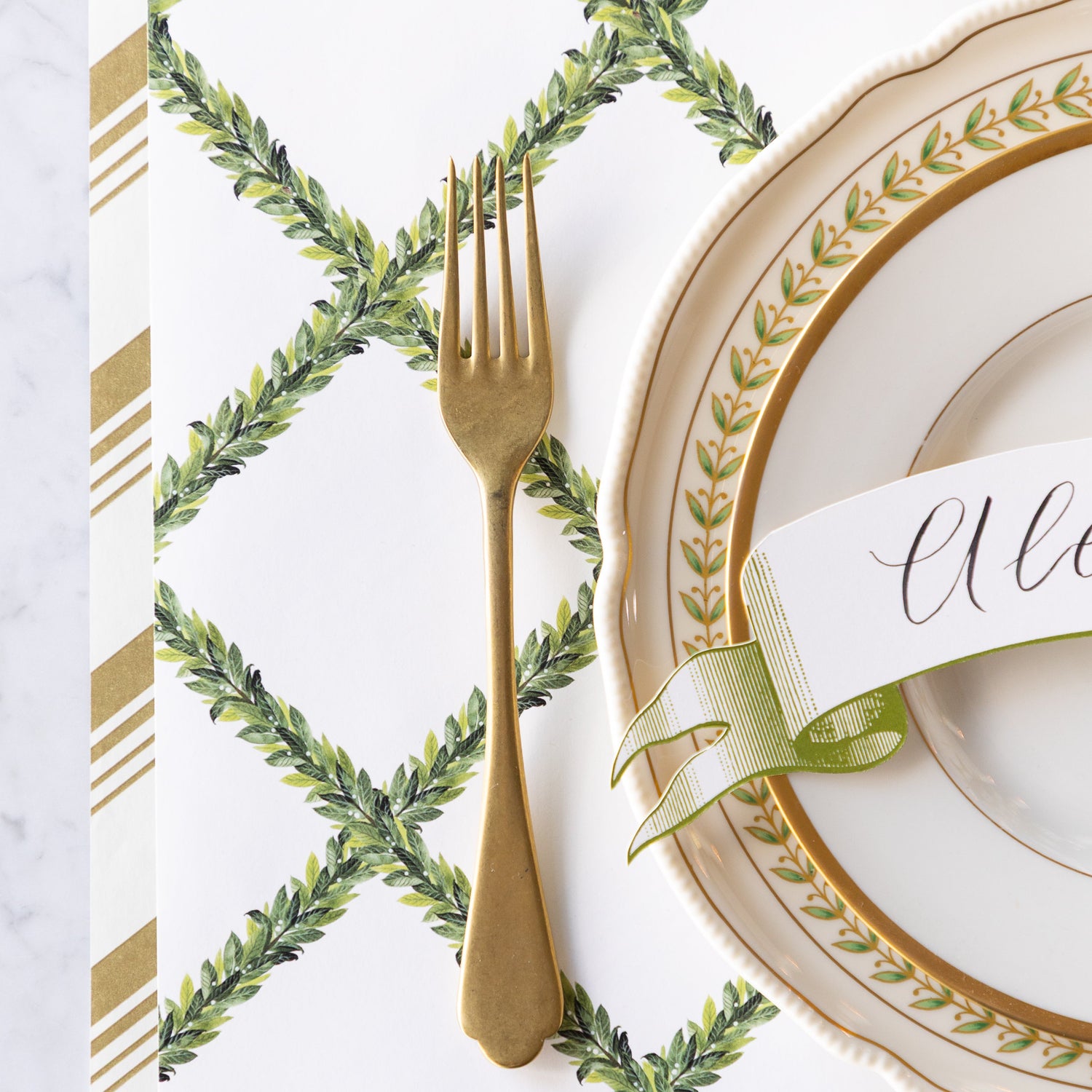 A place setting with vintage dinnerware and a gold fork on the Laurel Wreath Placemat and Gold Peppermint Stripe Runner underneath.