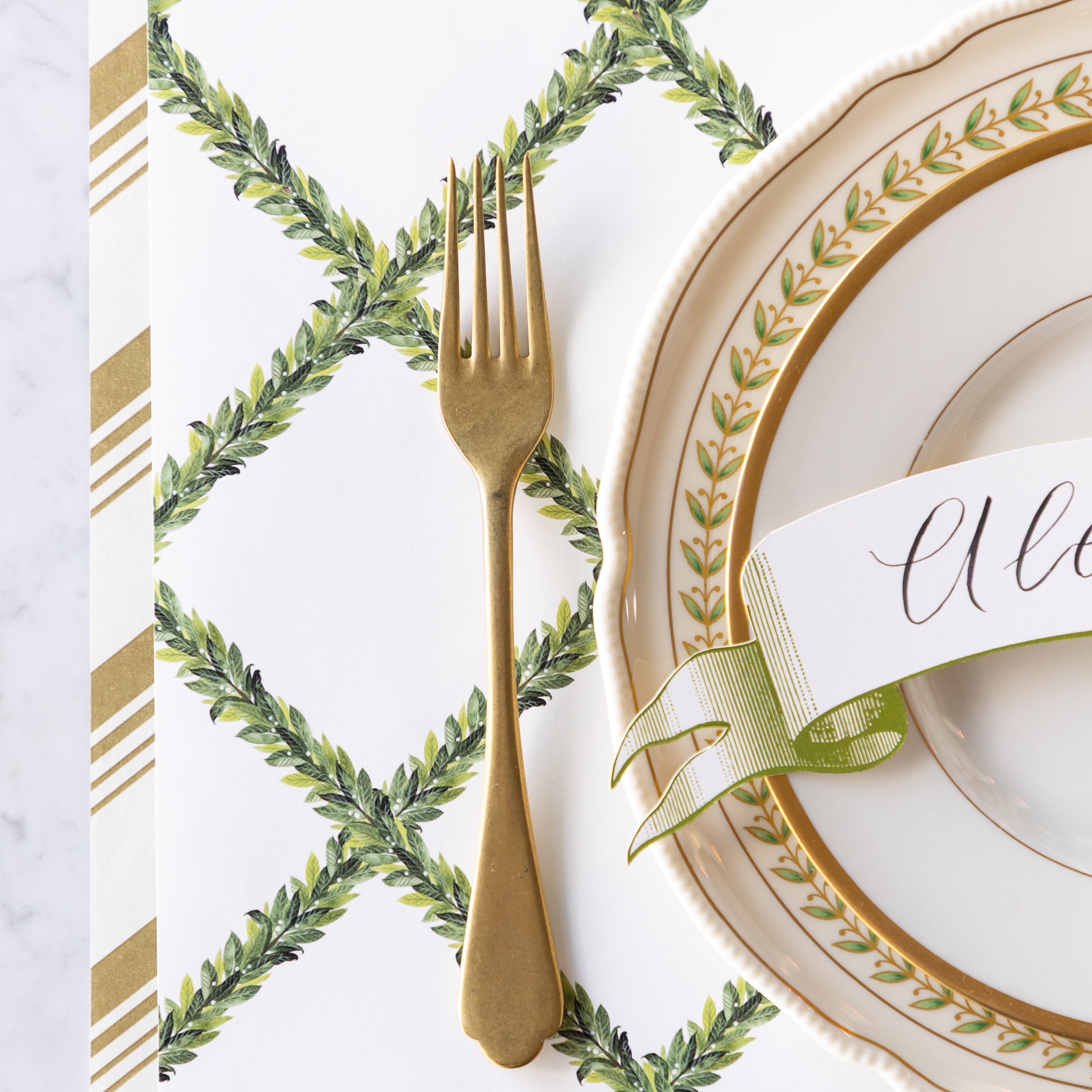 A place setting with vintage dinnerware and a gold fork on the Laurel Wreath Placemat and Gold Peppermint Stripe Runner underneath.