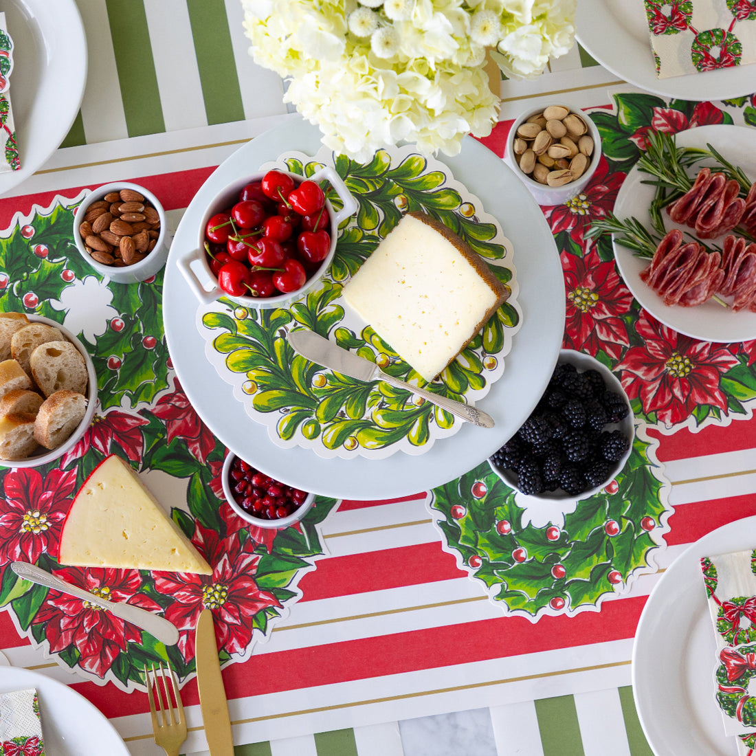 A table setting featuring the Holiday Wreath Serving Papers with various meats, cheeses, nuts and fruits atop.