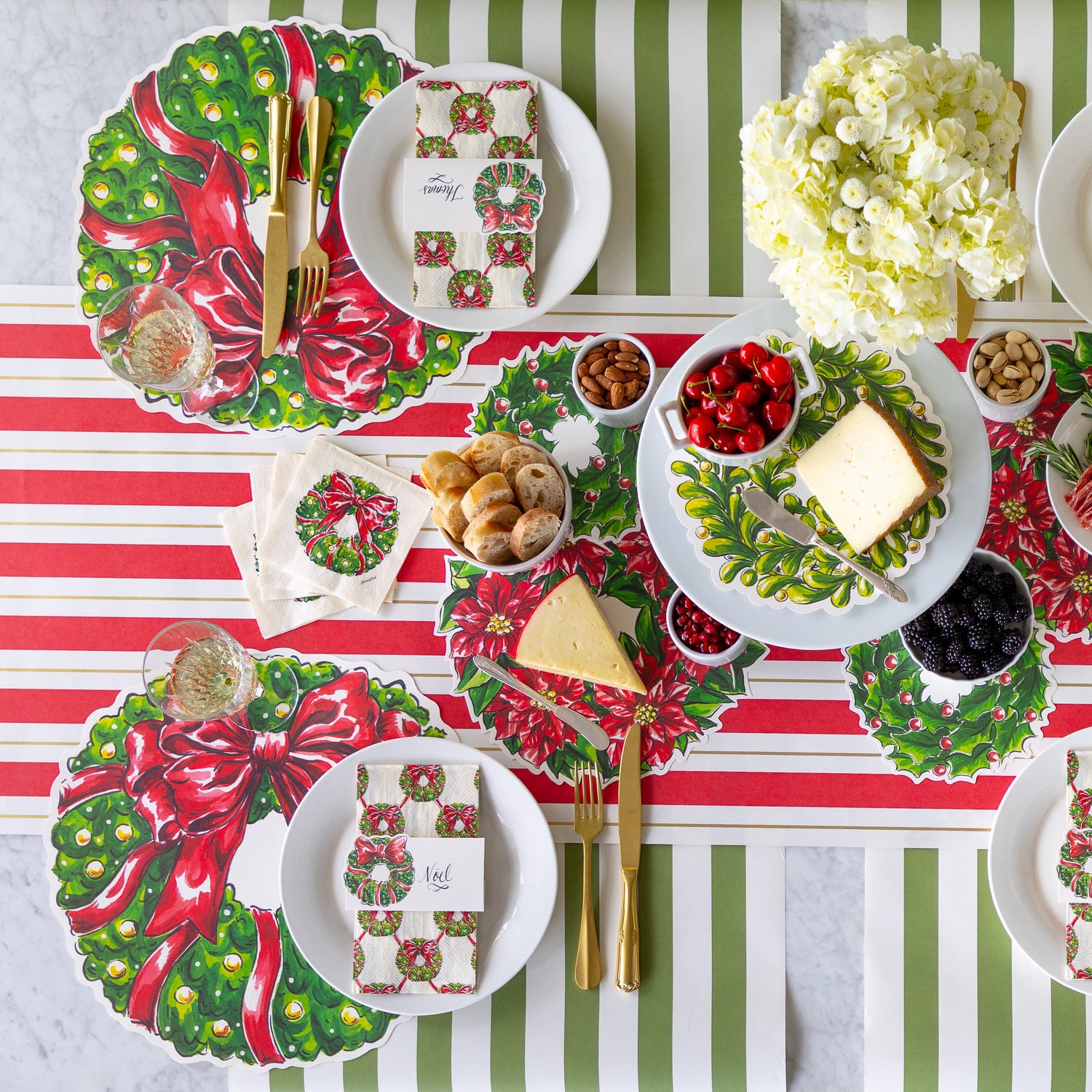 Festive holiday table setting with Die-Cut Holiday Wreath Placemats, gold cutlery, Holiday Wreath Napkins, place cards and serving papers, on the Red &amp; Gold Awning Stripe Runner and Moss Classic Stripe Runner.