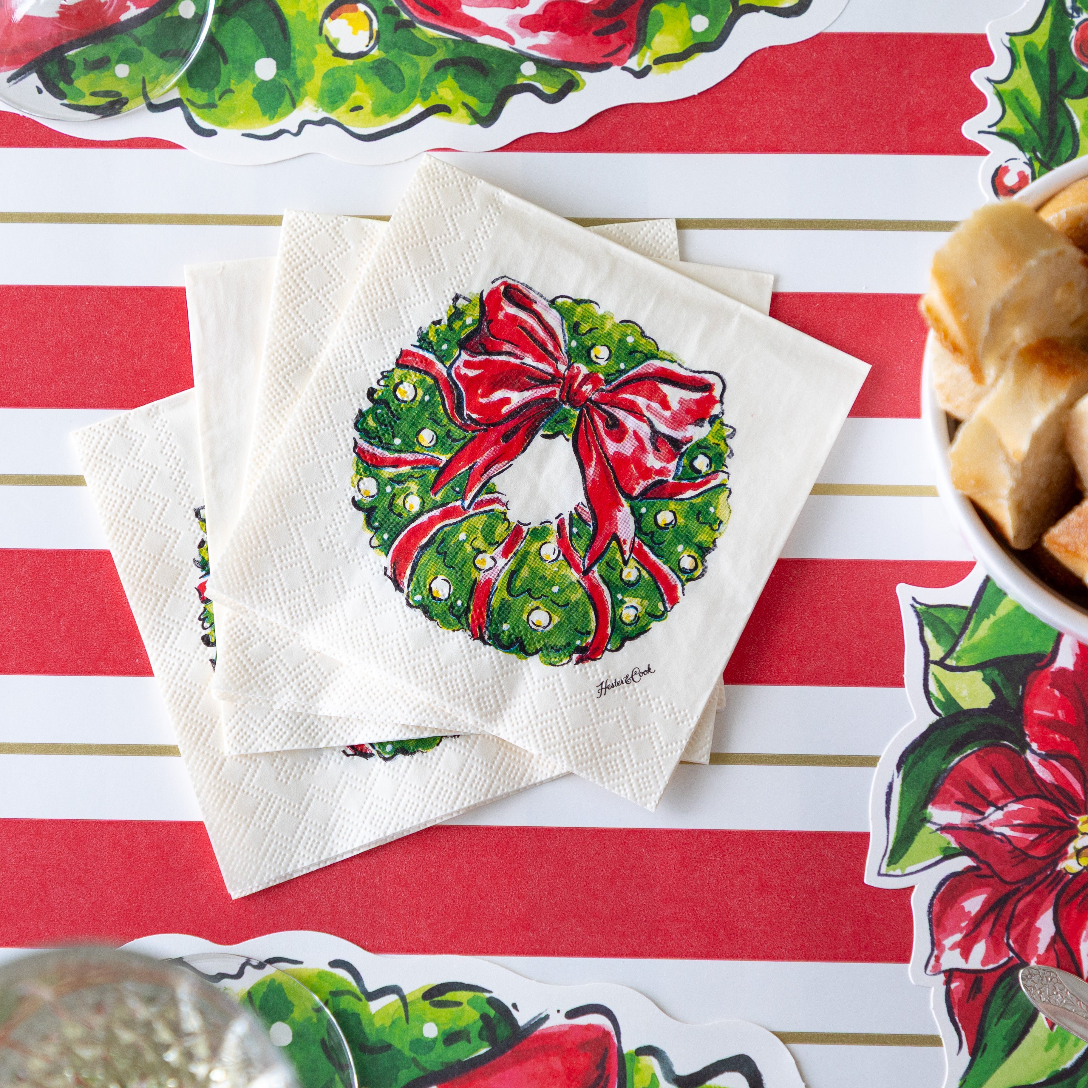 A fanned out stack of Holiday Wreath Cocktail Napkins on the Red &amp; Gold Awning Stripe Runner.