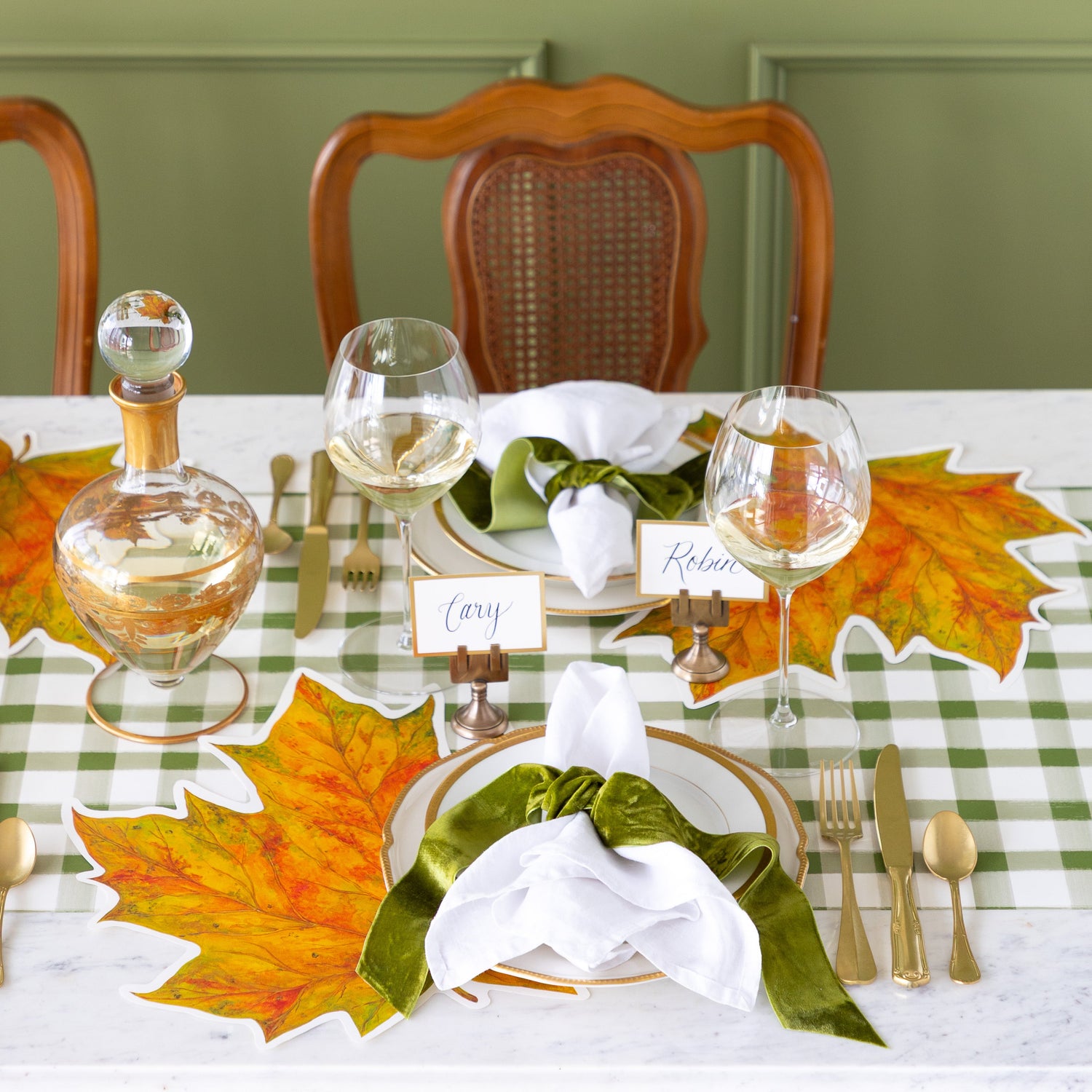 An elegant place setting featuring the Die-cut Fall Leaf Placemat, gold rimmed plates, the Gold Frame Place Card held by the Brass Place Card Holder, white napkins tied by a green velvet ribbon and the Green Painted Check Runner underneath.