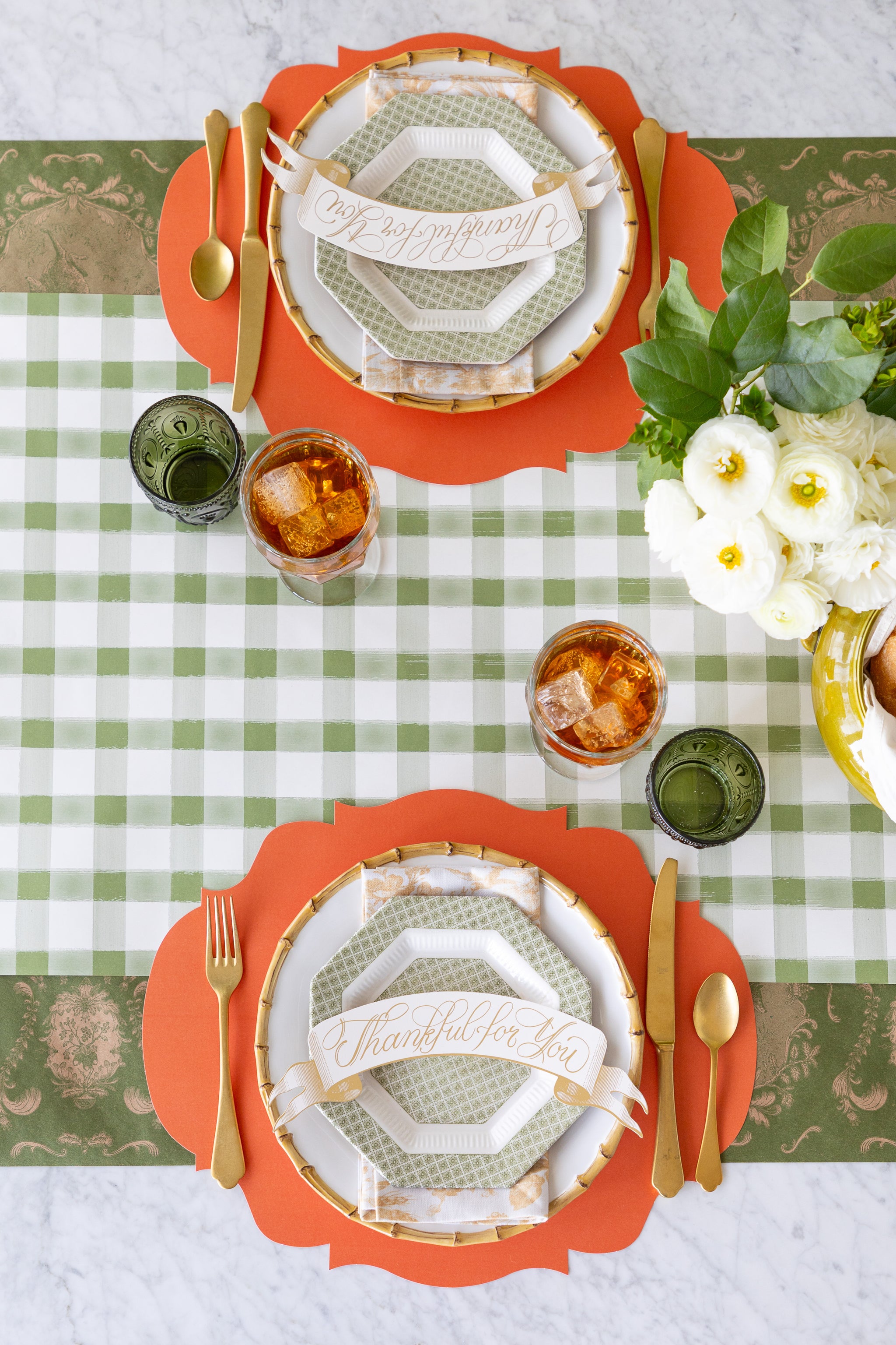 A table setting featuring the Die-cut Orange French Frame Placemats, Thankful For You Table Banner Table Accents, gold flatware and flowers on the Moss Painted Check and Moss Fable Toile Runners.
