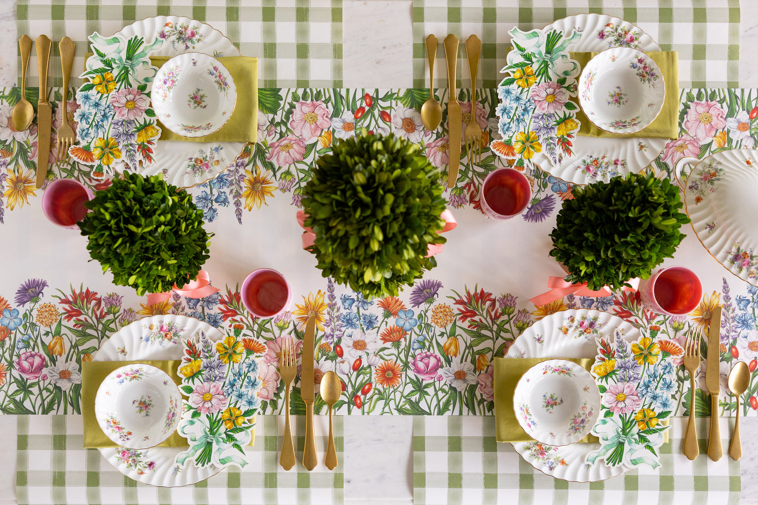 Dining table setting with floral table runner, plates, and cutlery on a checkered table runner.