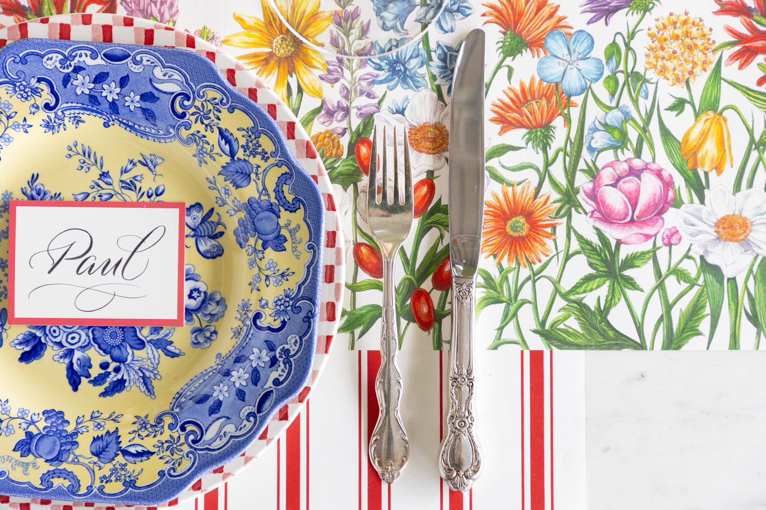Decorative table setting with floral placemat, blue and yellow plate, and silverware.