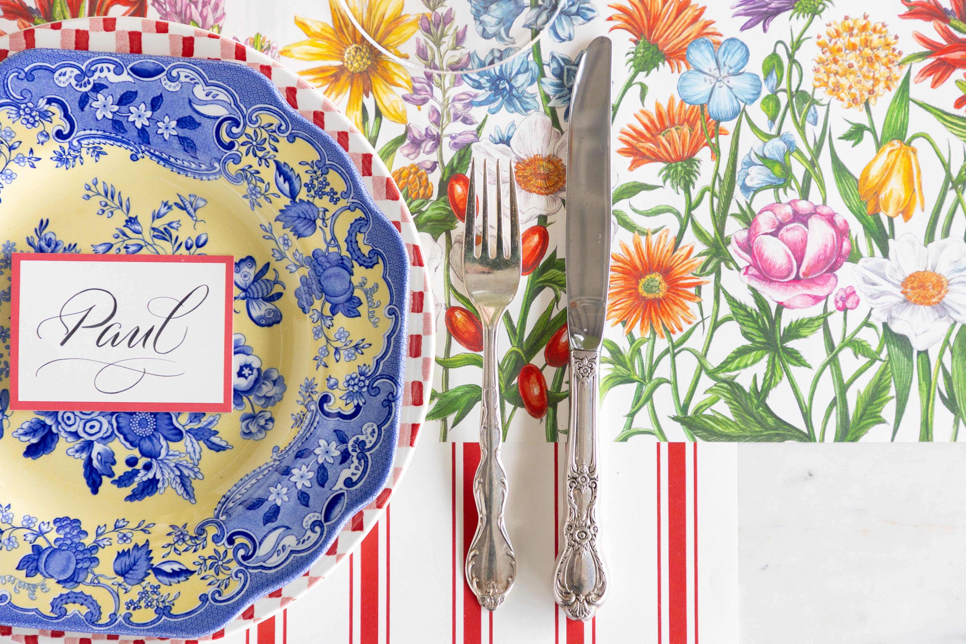 Decorative table setting with floral placemat, blue and yellow plate, and silverware.